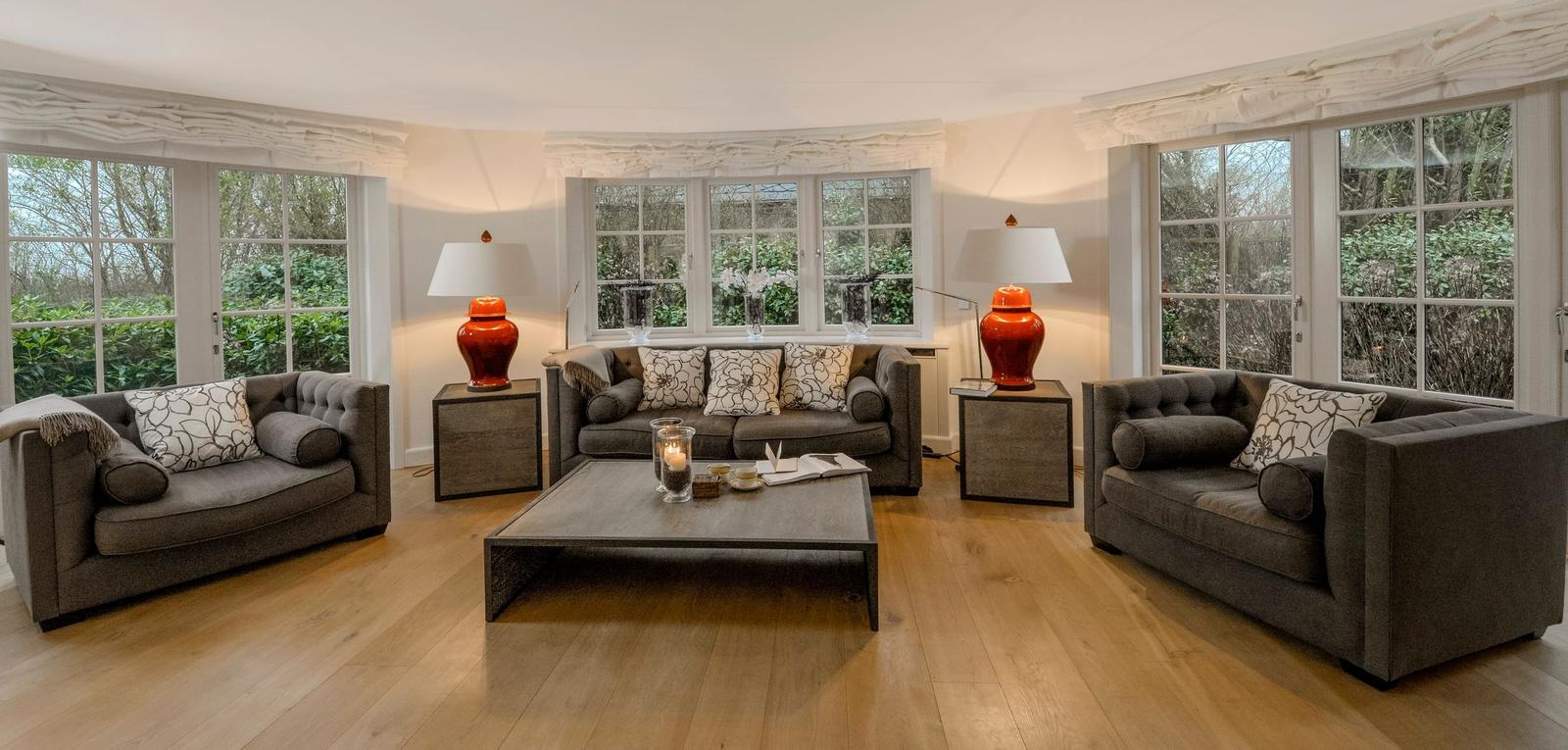 Wohnzimmer mit grauen Sofas, Holzboden und großen Fenstern.