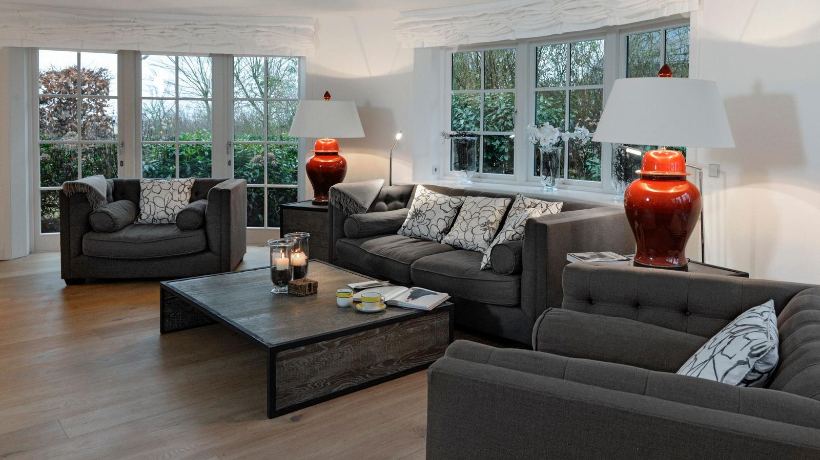 Wohnzimmer mit grauen Sofas, Holzboden und großen Fenstern.