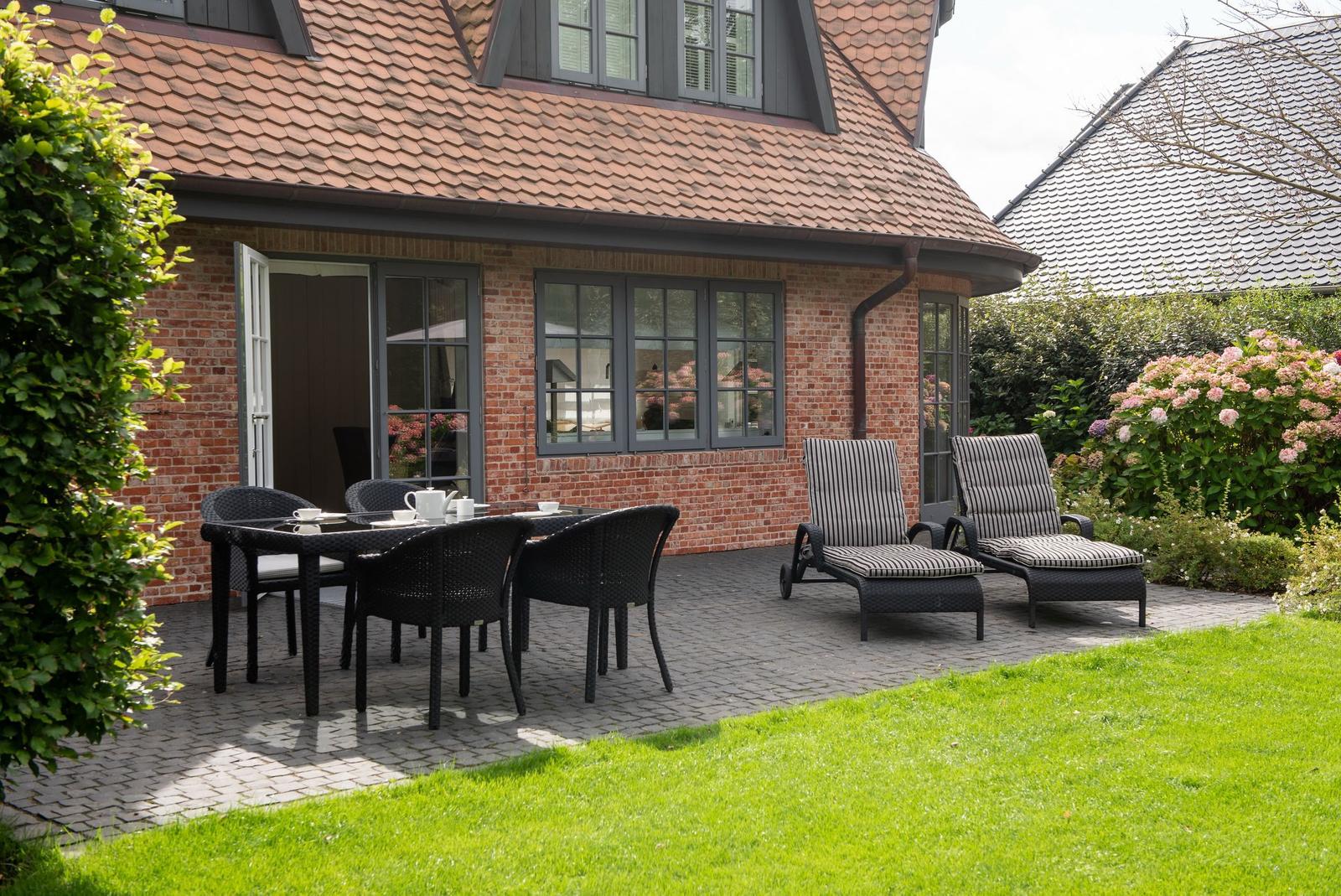 Terrasse mit Sitzgruppe und Garten. Haus mit Ziegeldach und Backsteinfassade.
