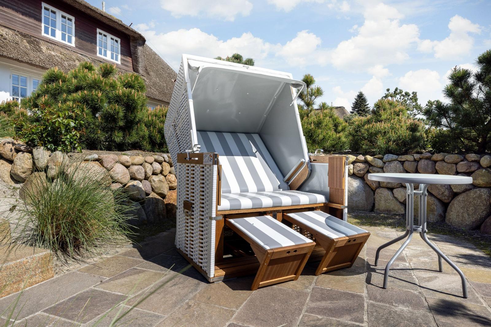 Hocker mit Streifen, Tisch und Steinterrasse vor einem Haus
