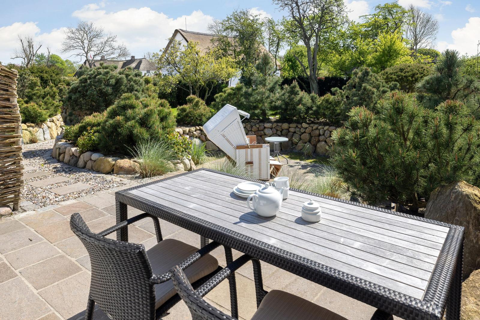Terrasse mit Tisch und Stühlen, umgeben von Grünflächen und Steinmauern.