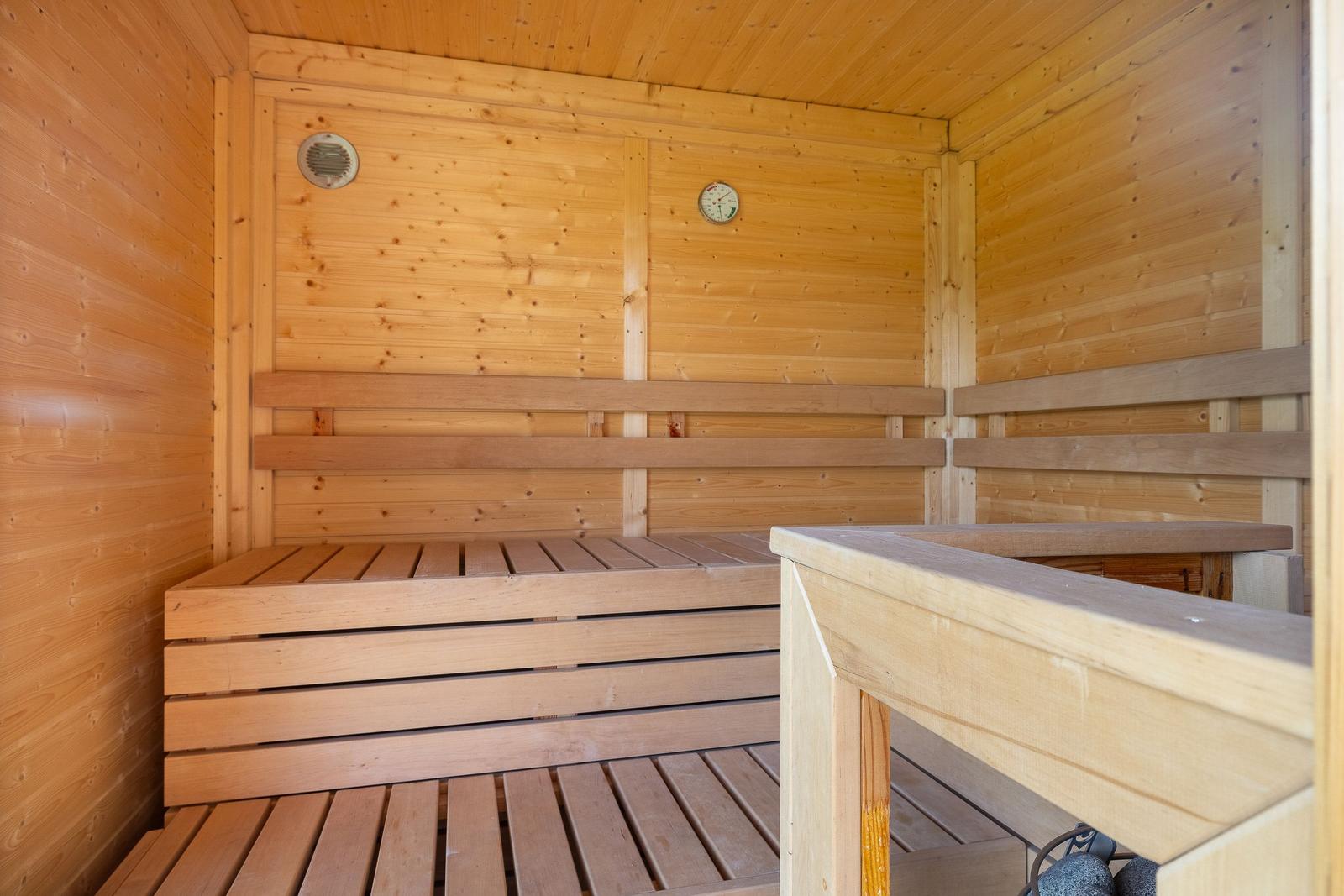 Holzsauna mit Sitzbänken und Temperaturuhr an der Wand.