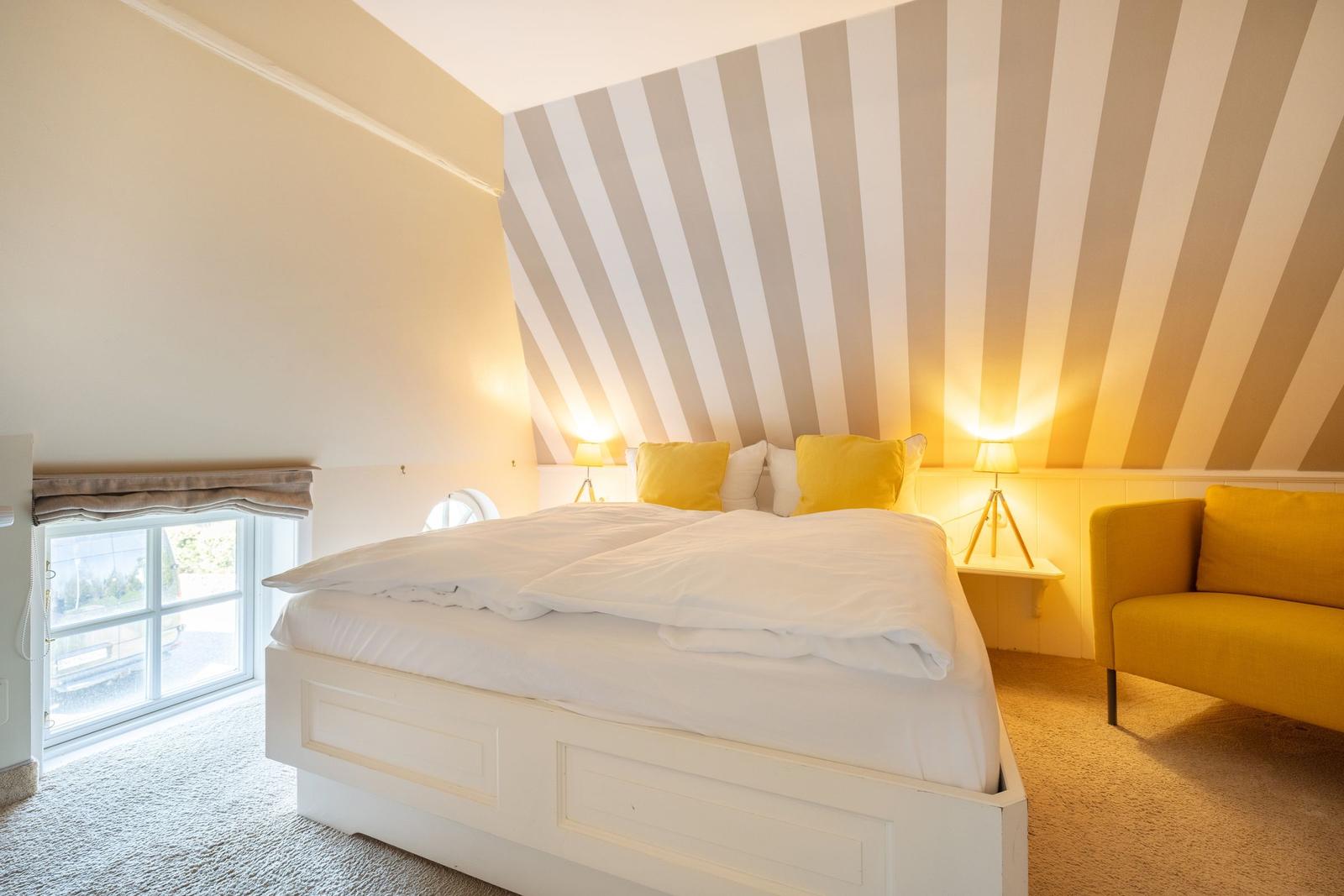 Schlafzimmer mit Bett, gelben Kissen und gestreifter Wand