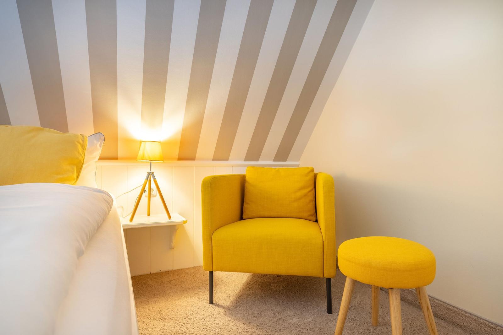 Schlafzimmer mit gelber Sitzgelegenheit und gestreifter Decke.