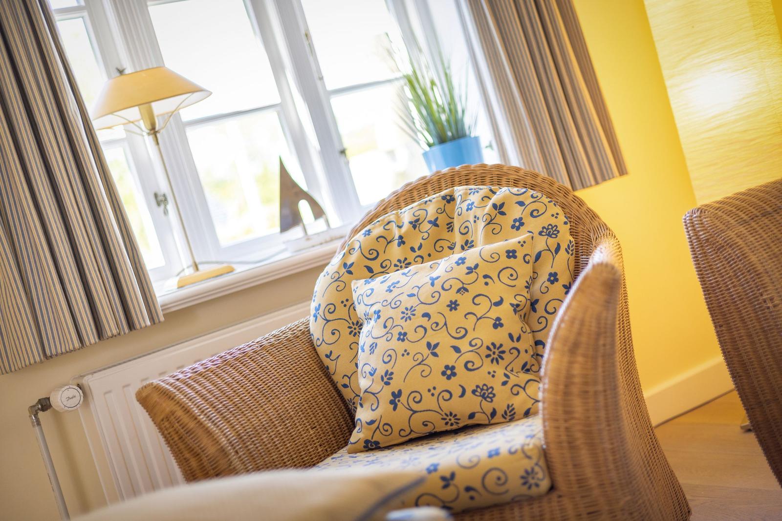 Wicker-Sofa mit blau-gelben Kissen vor Fenster mit Vorhängen.