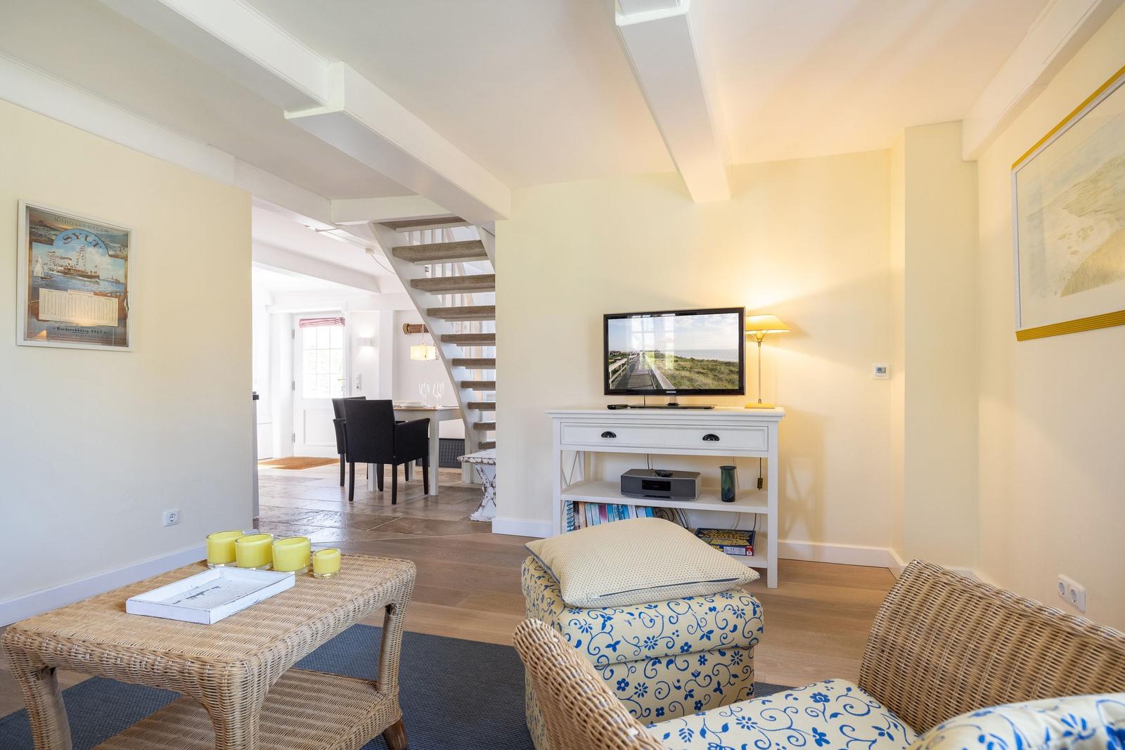 Wohnzimmer mit Fernseher, Sessel und Treppe zur Küche.