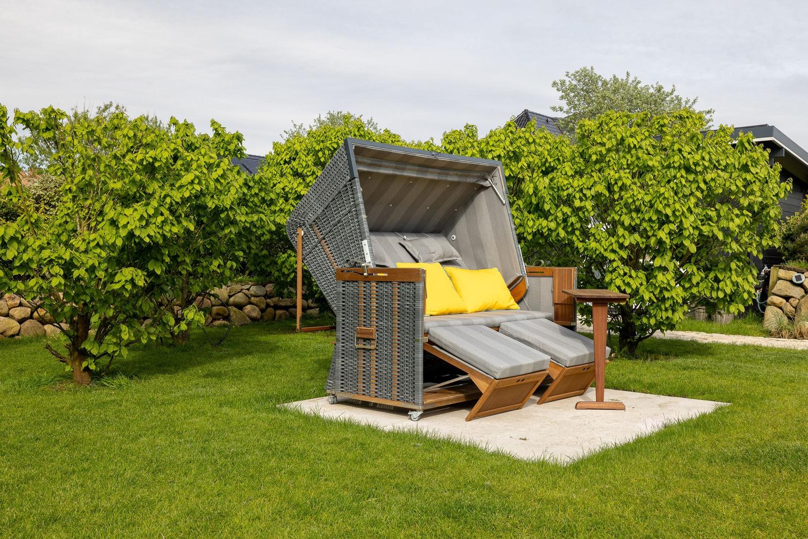 Außenliegender Rattan-Schirm mit Sitzbereich und gelben Kissen auf einer Terrasse.