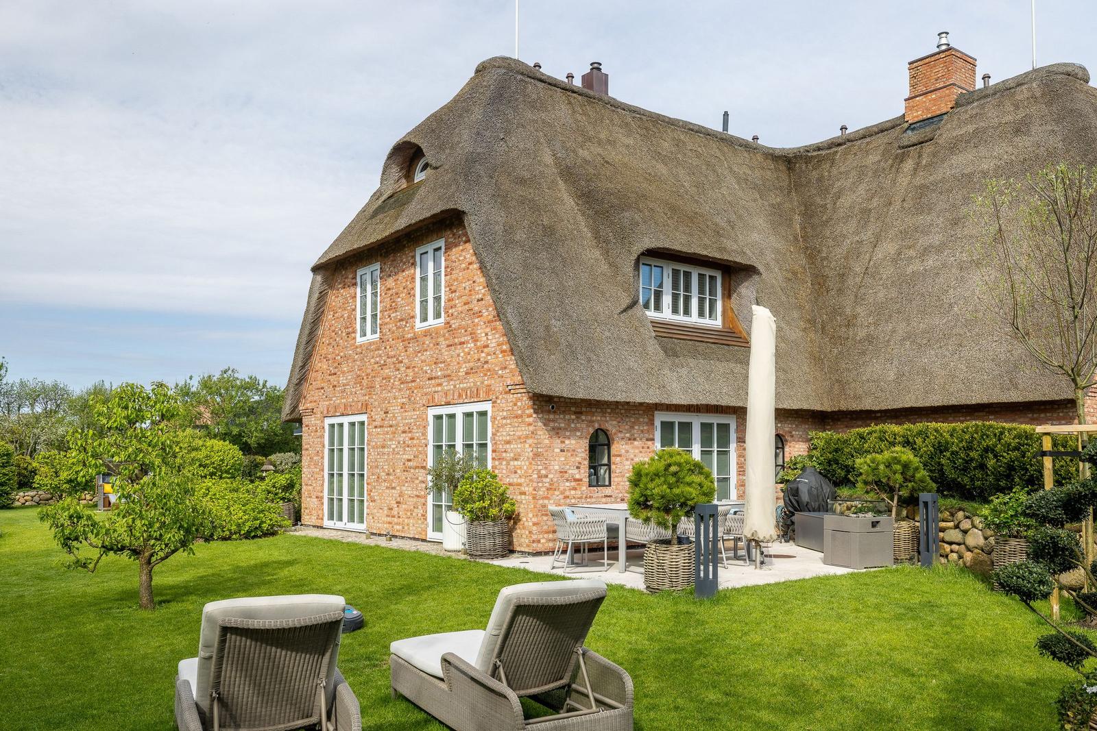 Haus mit Strohdach, Garten und Außensitzgelegenheiten.
