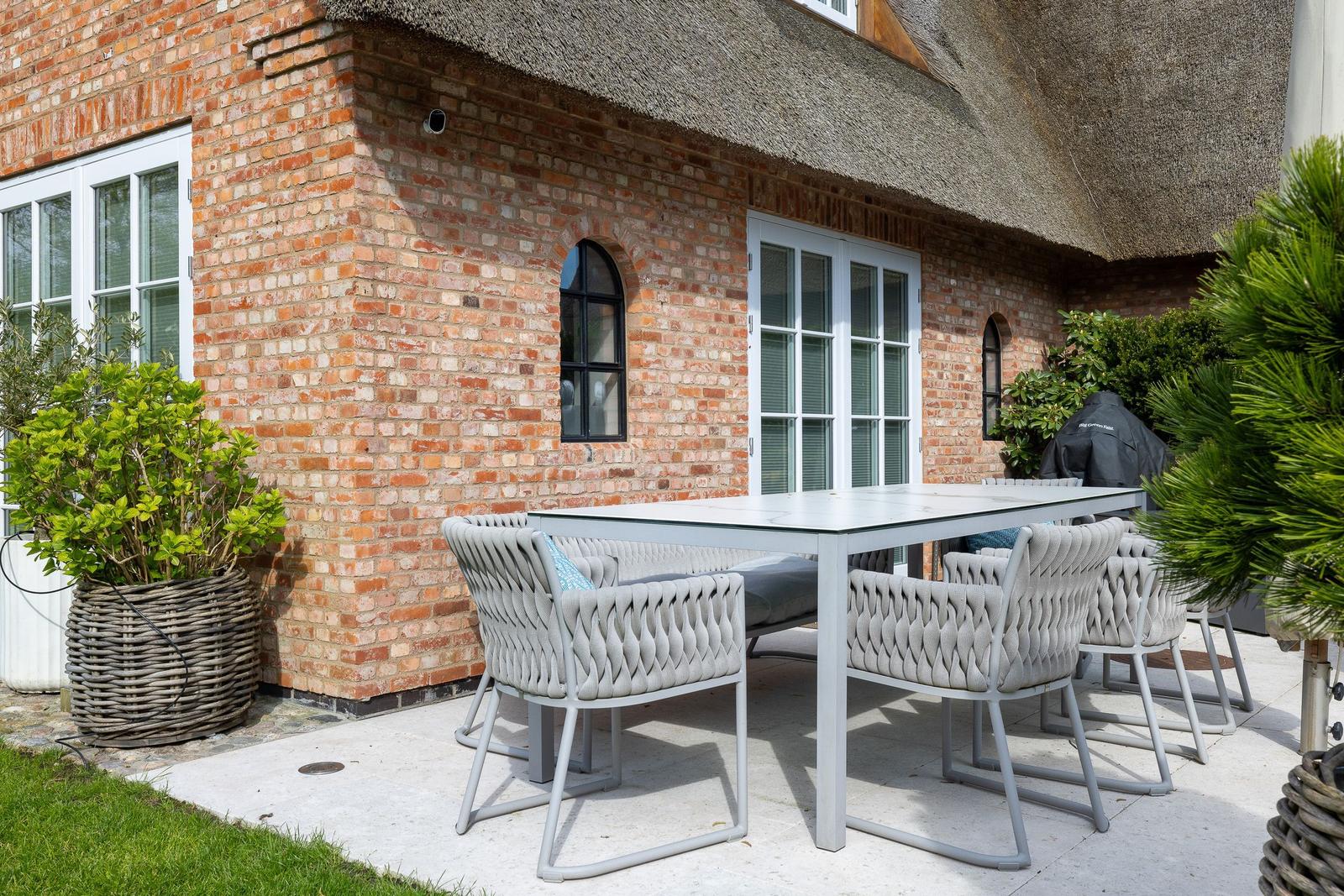 Terrasse mit Tisch und Stühlen vor Backsteinhaus mit Strohdach