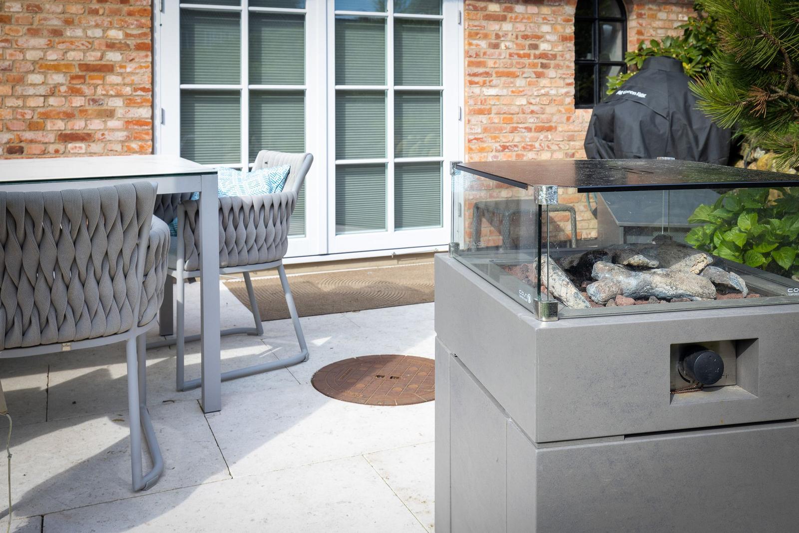 Terrasse mit Sitzgruppe und Feuerkamin. Hintergrund: Haus mit Backsteinwand und Fenstern.