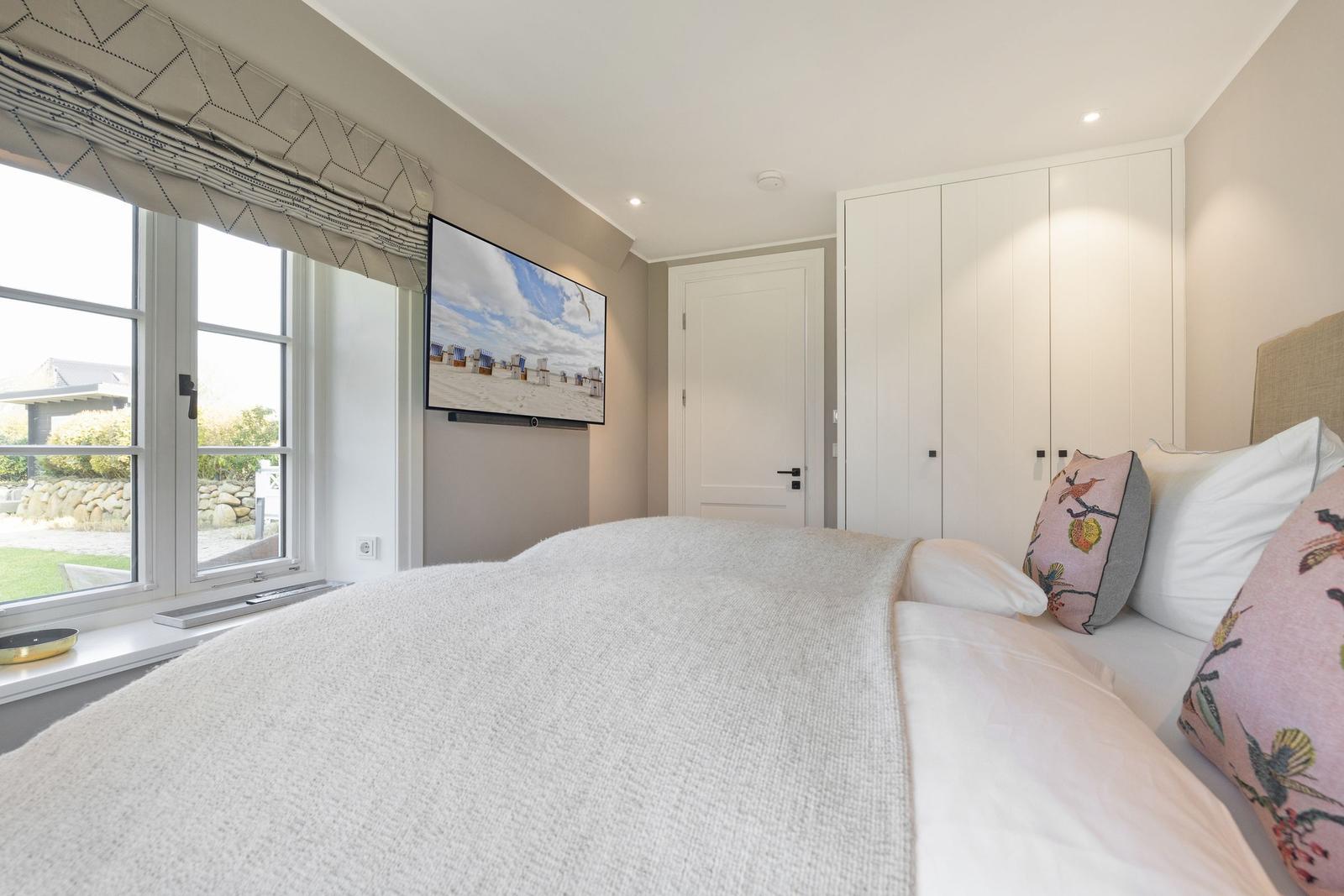 Schlafzimmer mit Bett, Fernseher und Fenster mit Blick auf Garten.