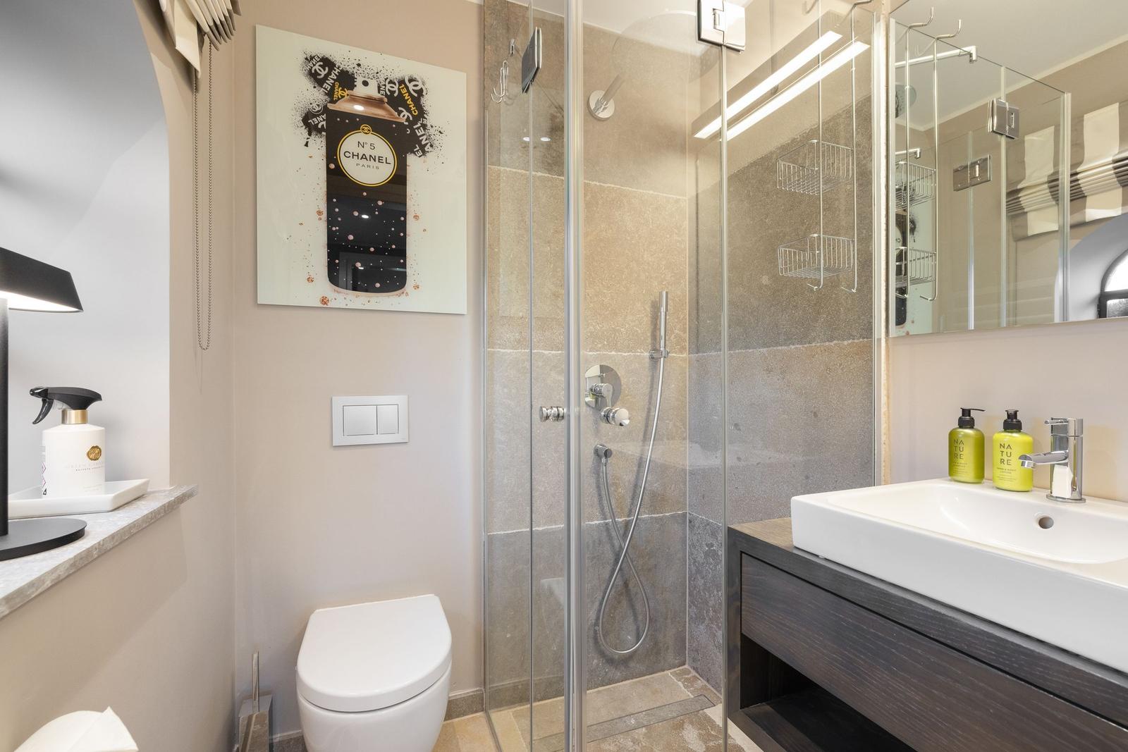 Badezimmer mit Dusche, Waschbecken und Toilette. Wandbild und Handtücher sichtbar.