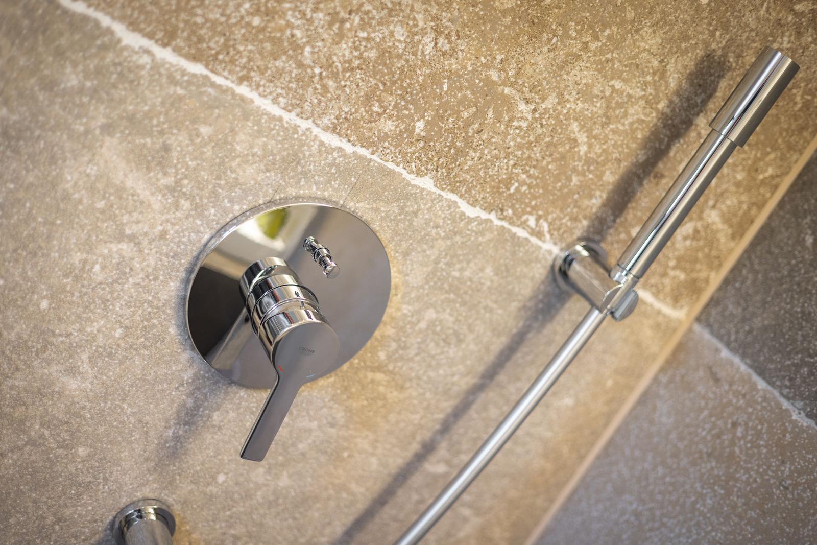 Duschbereich mit Chromarmatur und Handbrause an Steinwand