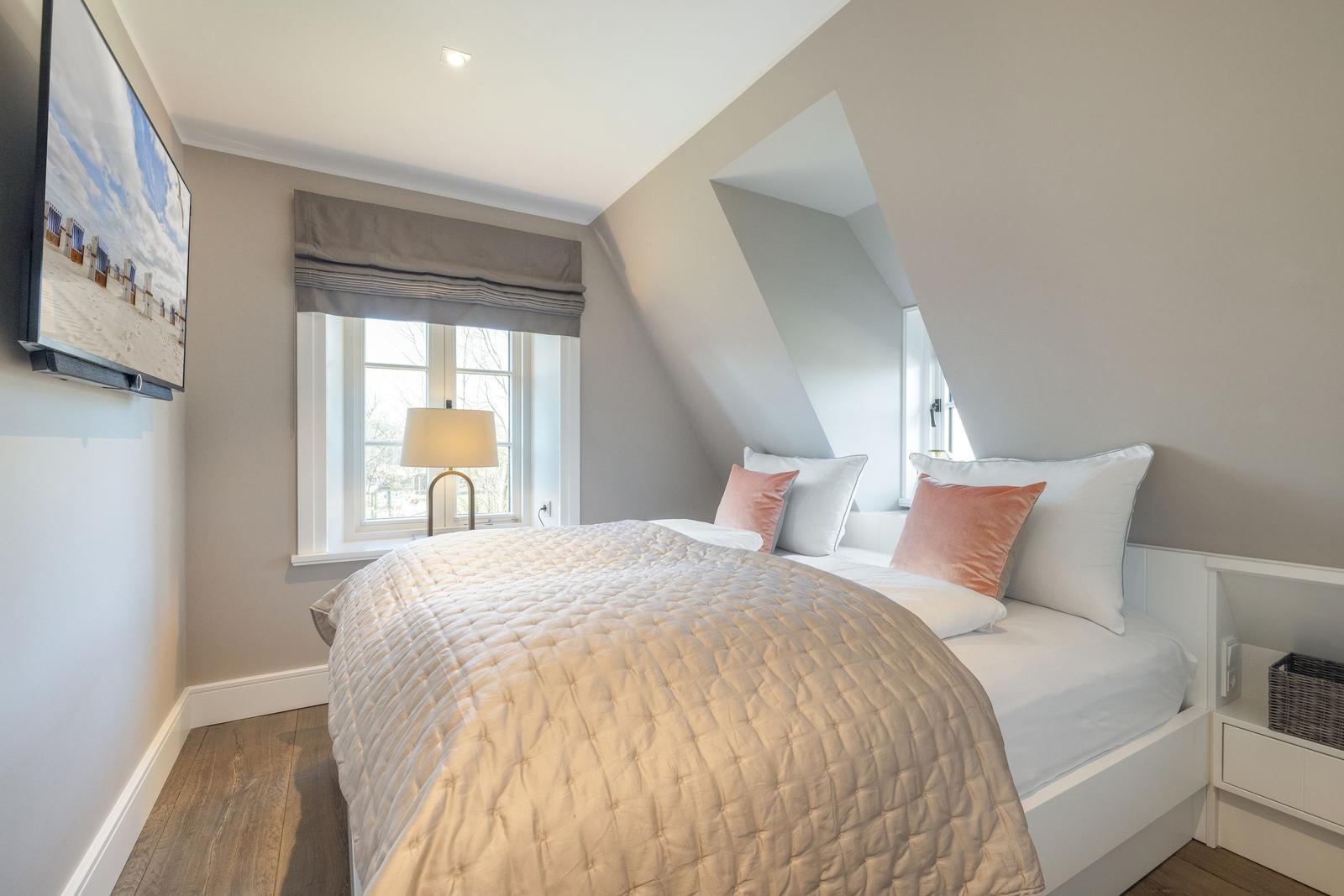 Schlafzimmer mit Dachschrägen, Bett mit Kissen und Fenster.