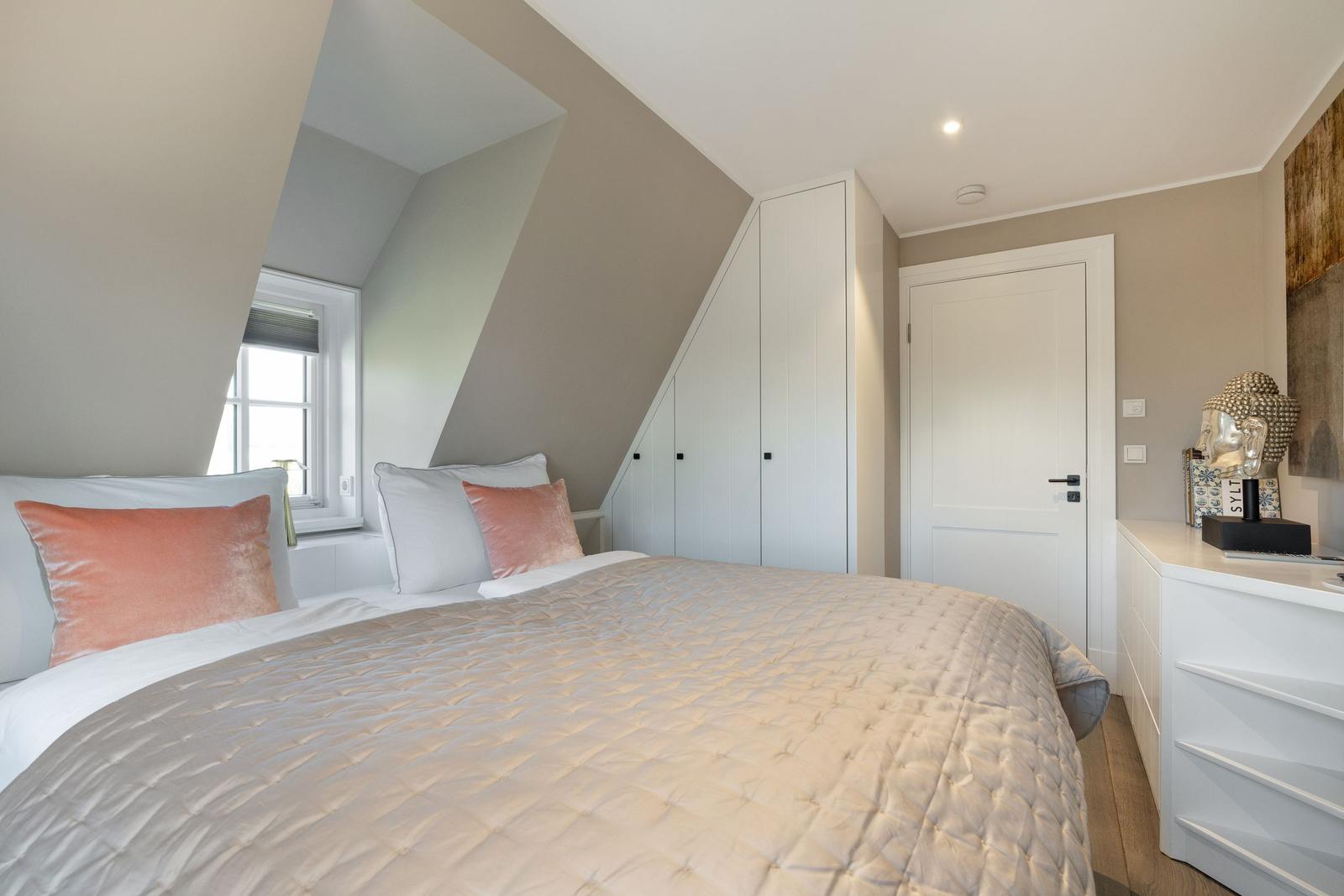 Schlafzimmer mit Dachschrägen, Bett, Kleiderschrank und Schminktisch.