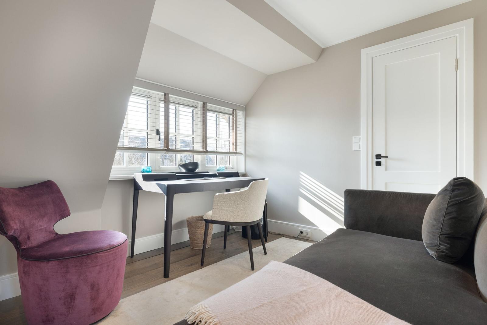 Zimmer mit Schreibtisch, Sofa und lila Sessel unter Dachschrägen.