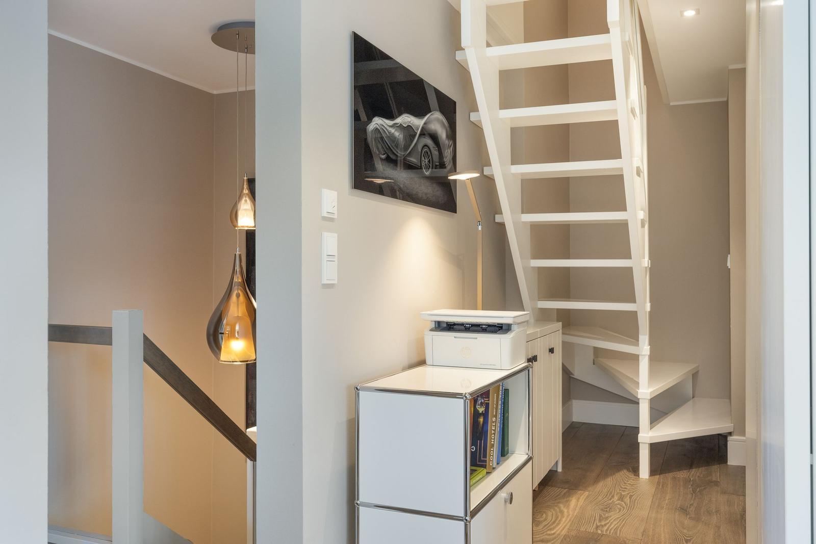 Haus mit weißen Treppen und moderner Beleuchtung. Auf einem Schrank steht ein Drucker.
