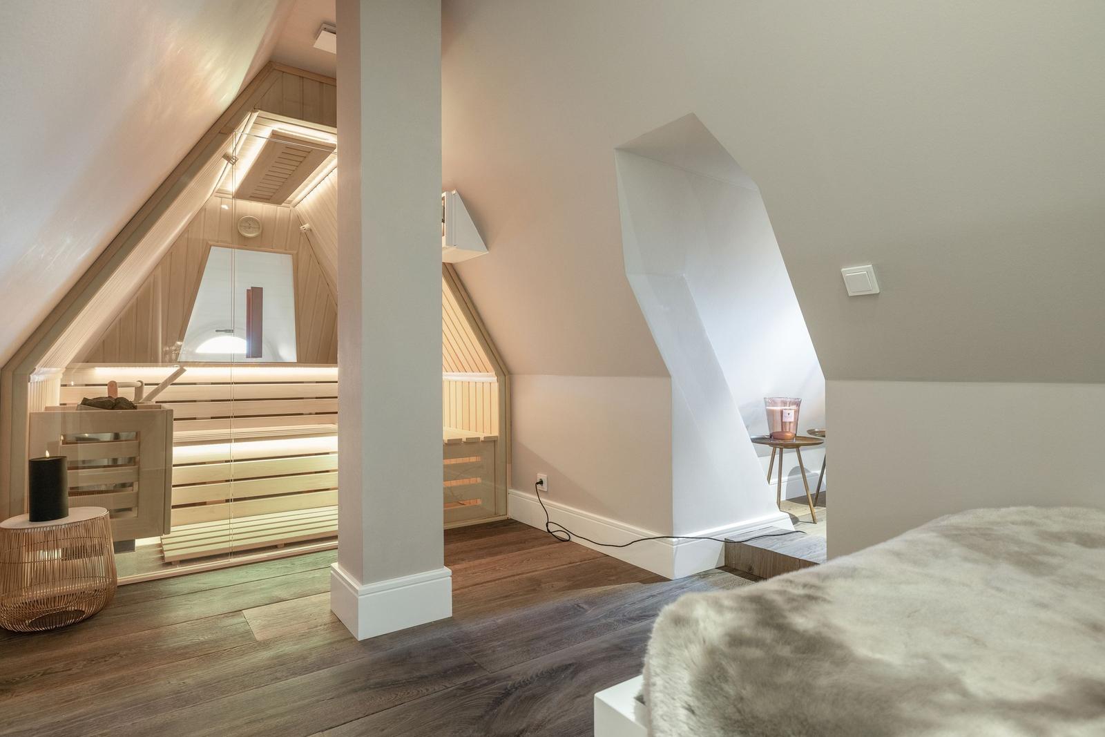 Dachgeschosszimmer mit Sauna und Bett. Holzfußboden und weiße Wände.