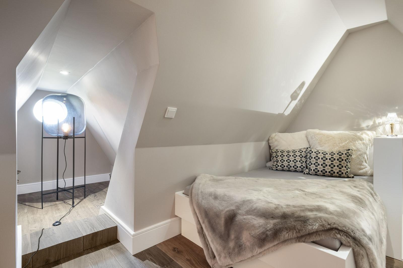Ein Schlafzimmer mit Dachschräge, Bett mit Decke und Kissen, Stehlampe und Holzboden.
