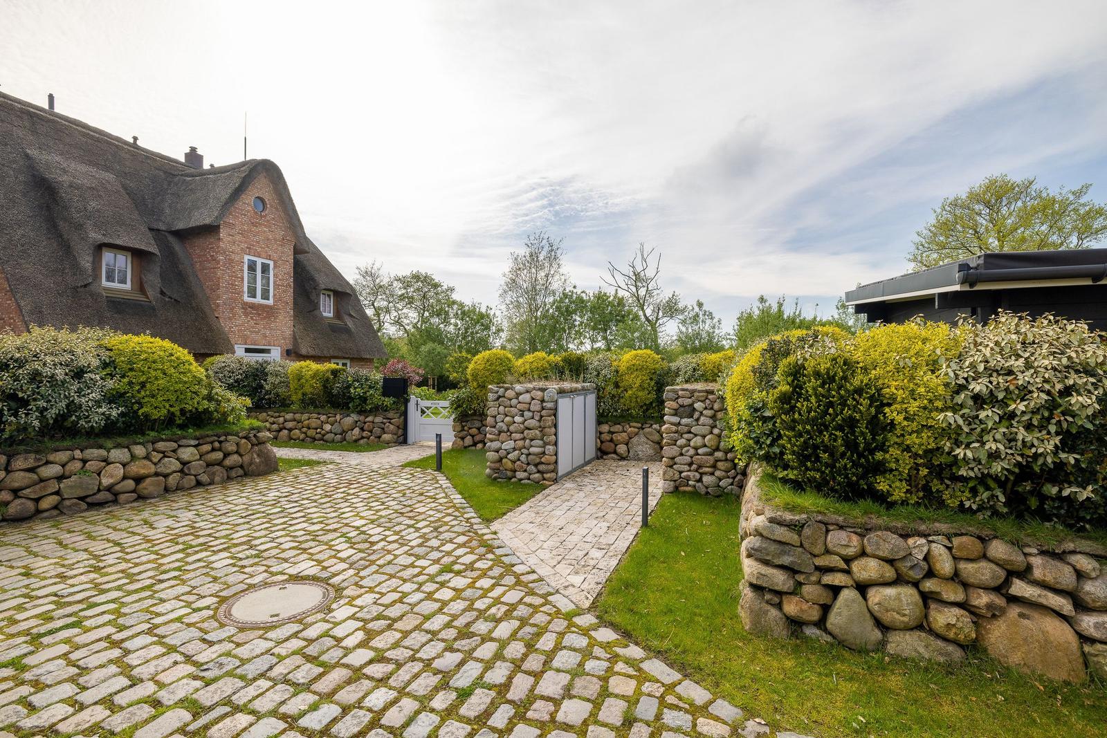 Haus mit Strohdach, Kiesweg und Steinmauern im Garten.