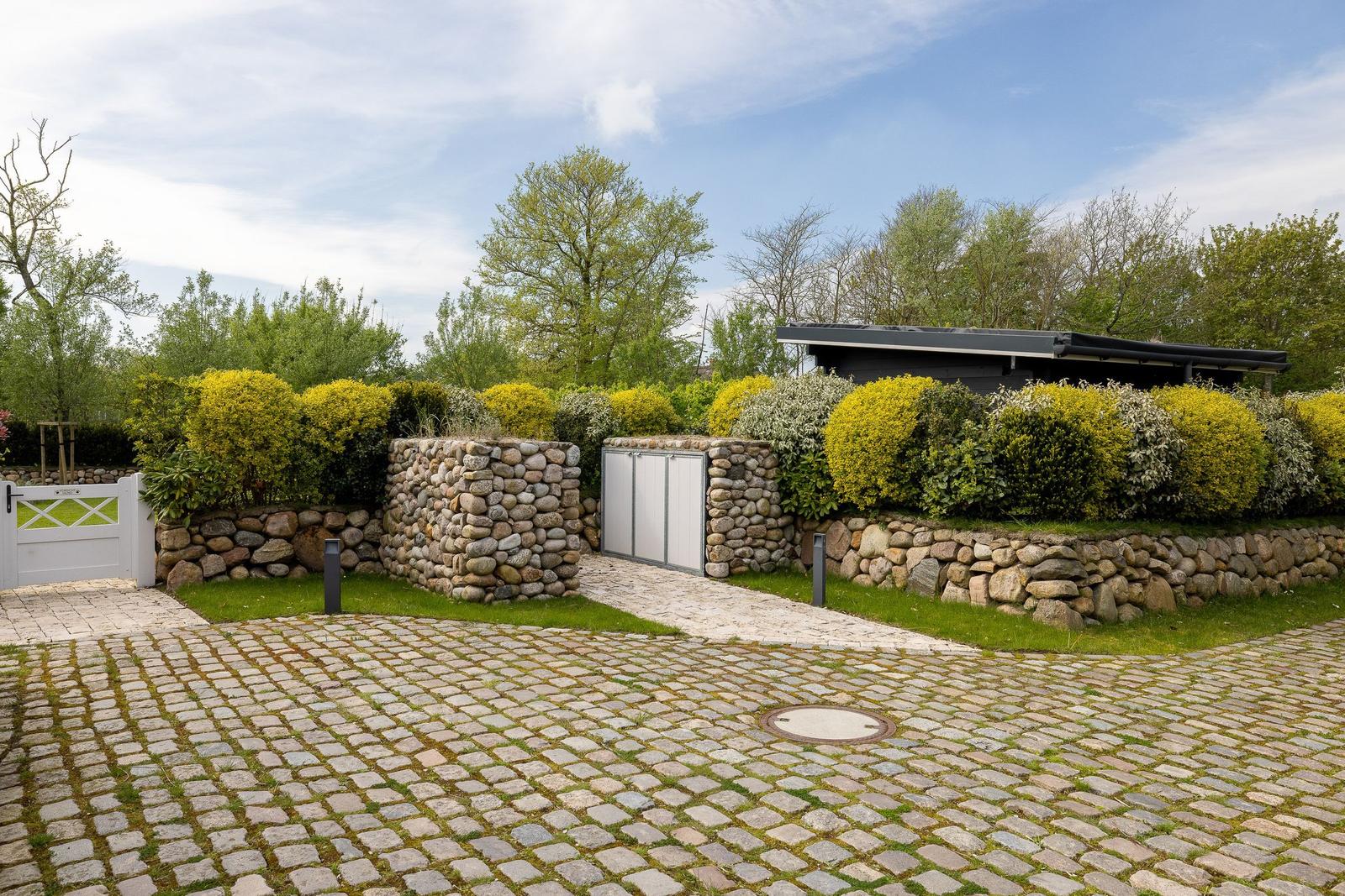 Steinmauer umgeben von grünen Büschen und einem Kiesweg.