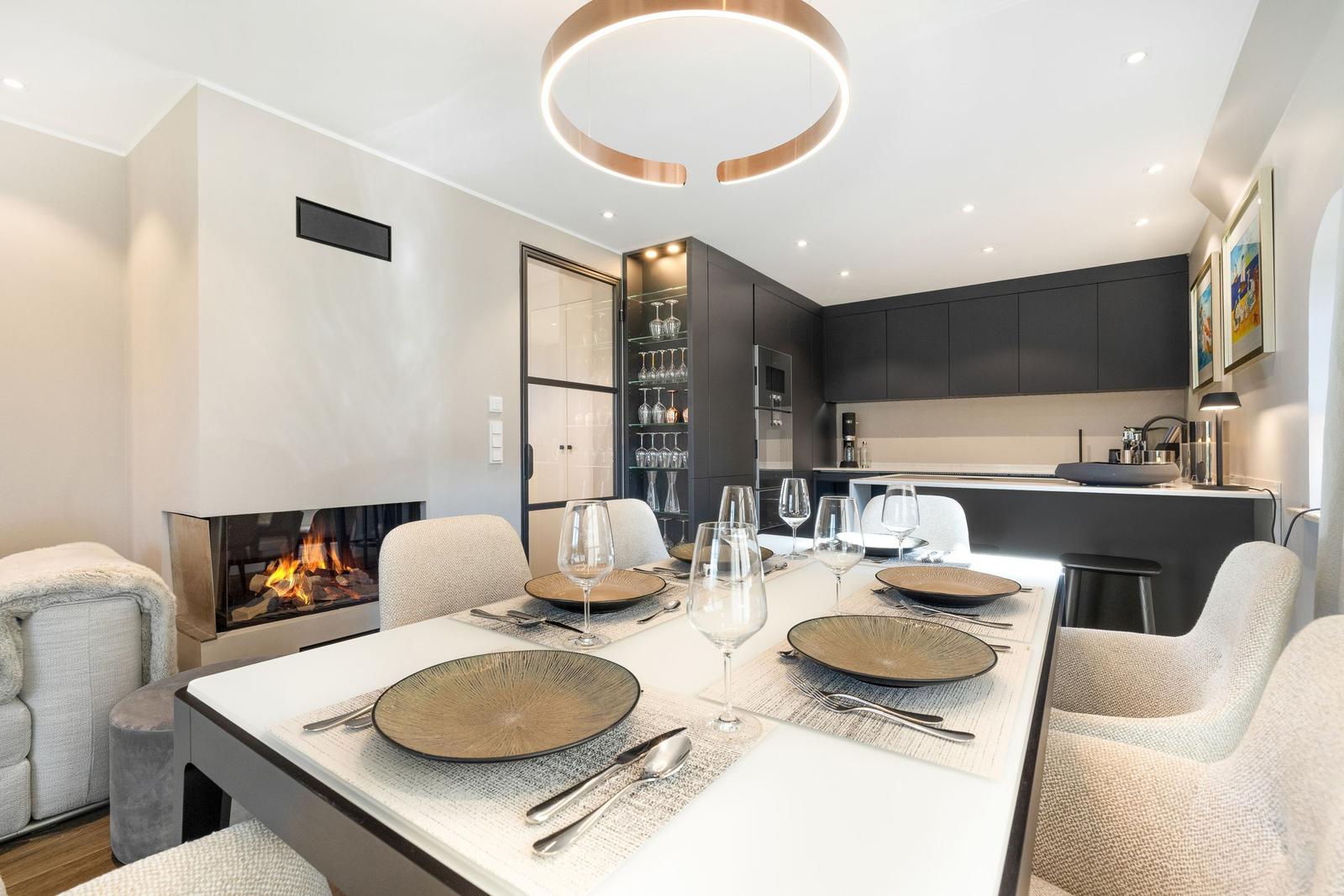 Esszimmer mit Esstisch, Stühlen und Kamin. Küche mit dunklen Schränken und Glasregal.