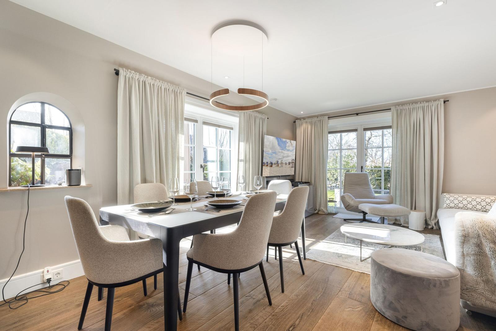 Esszimmer mit Tisch, Stühlen und Fenstern. Wohnbereich mit Sofa, Sessel und Couchtisch.