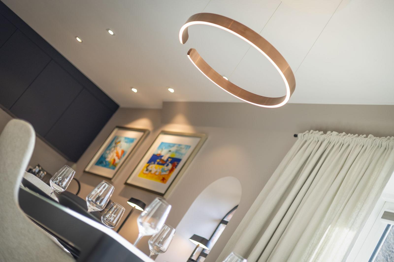 Moderne Esszimmer mit Glasplatte, Weinflaschen und stilvoller Deckenleuchte.