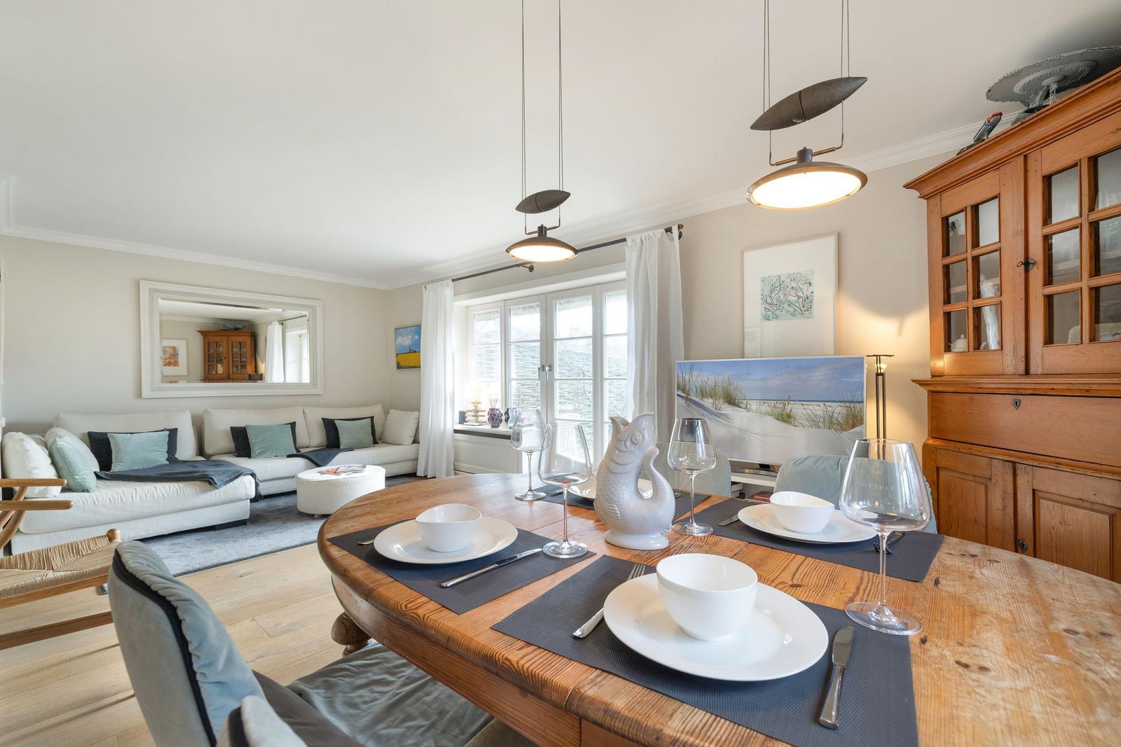 Dining room with wooden table, chairs, and window view. Living area with sofa and mirror.