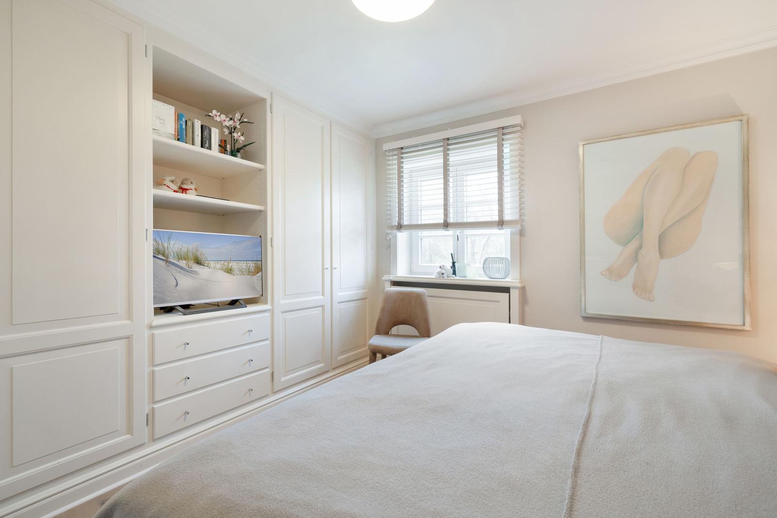 Bedroom with white wardrobe, TV, and bed. A large picture hangs on the wall.