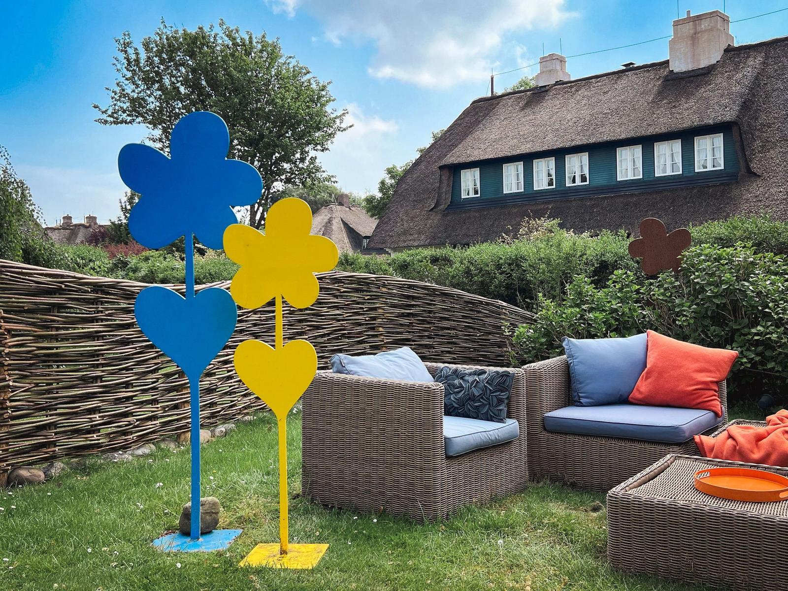 Garden with wicker furniture and colorful flower figures in front of a thatched house.