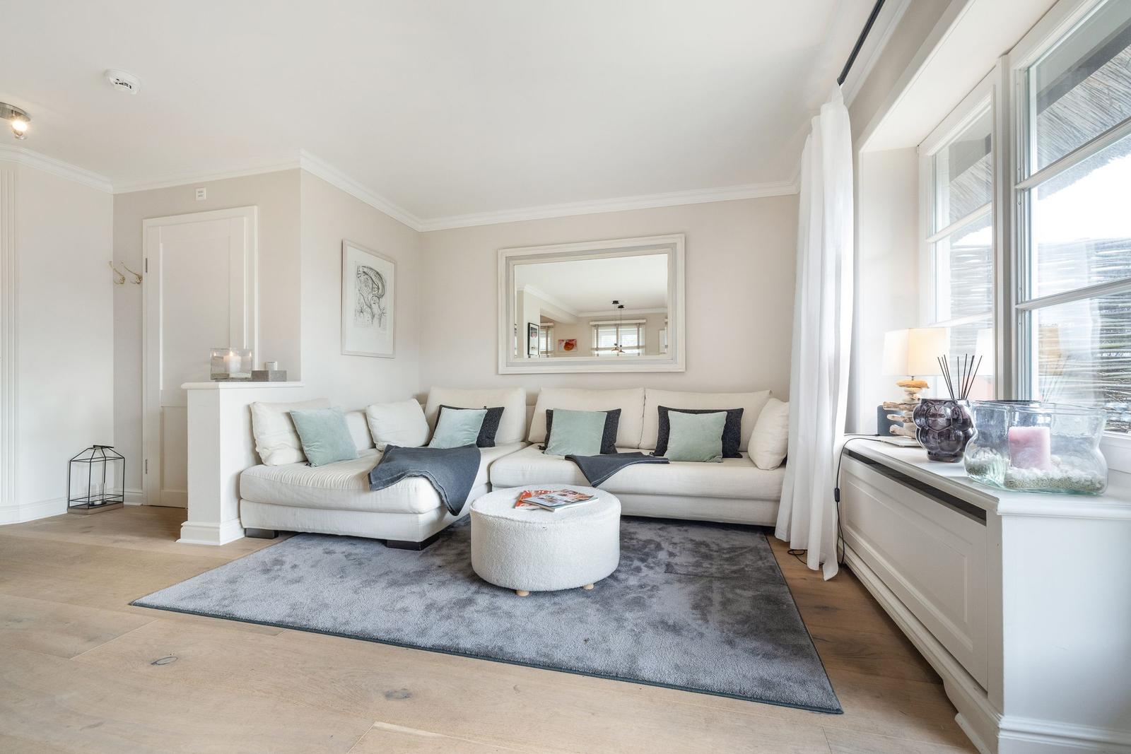 Living room with white sofa, round ottoman, and window sill.