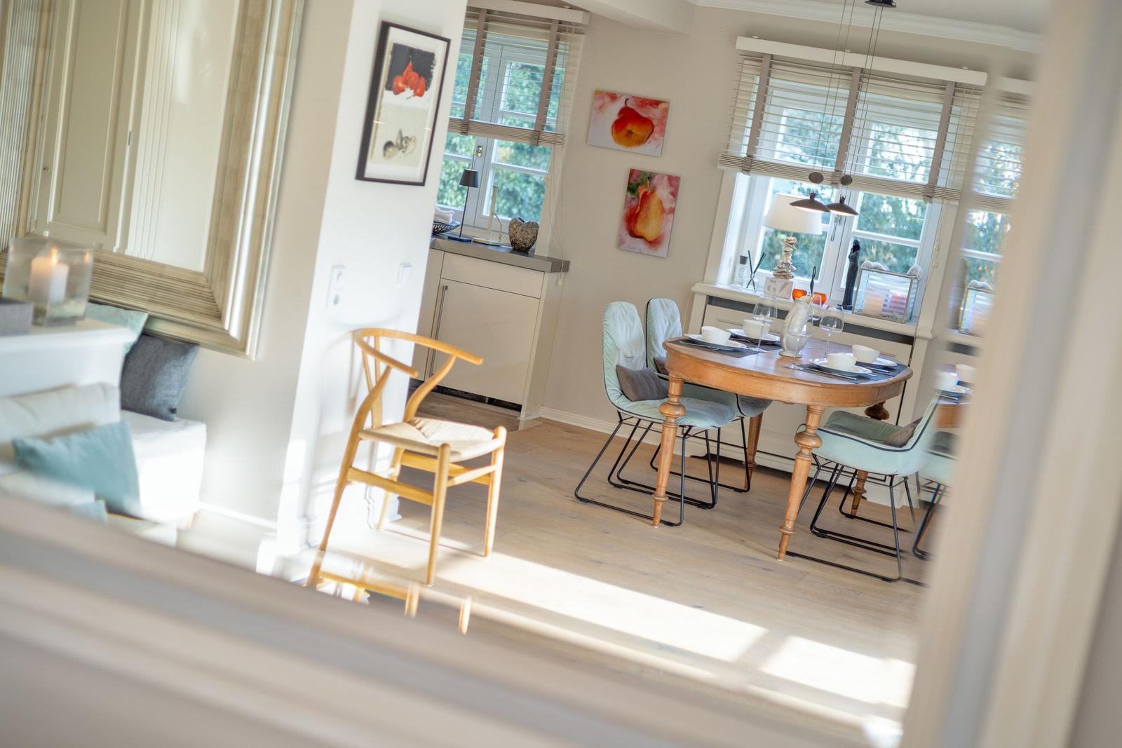 Dining room with wooden table and chairs, windows with blinds, wall art, and living area in background.