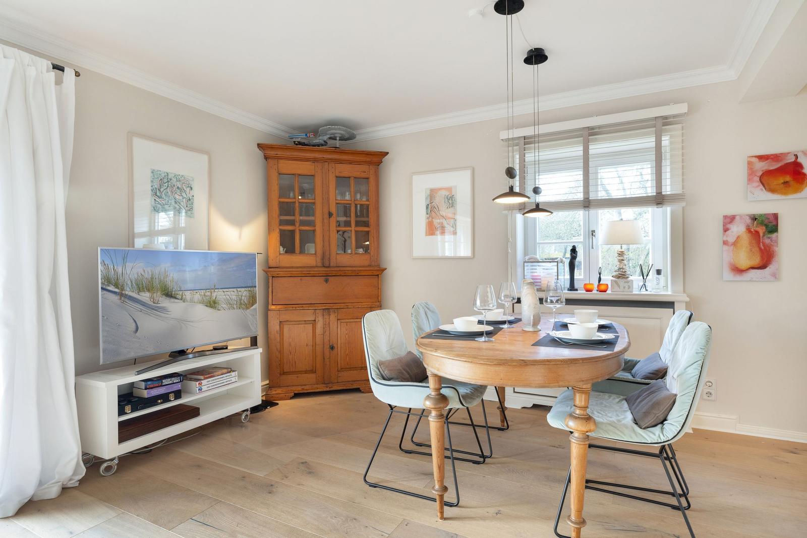 Dining room with round table, chairs, and TV. Wooden furniture and window with blinds.