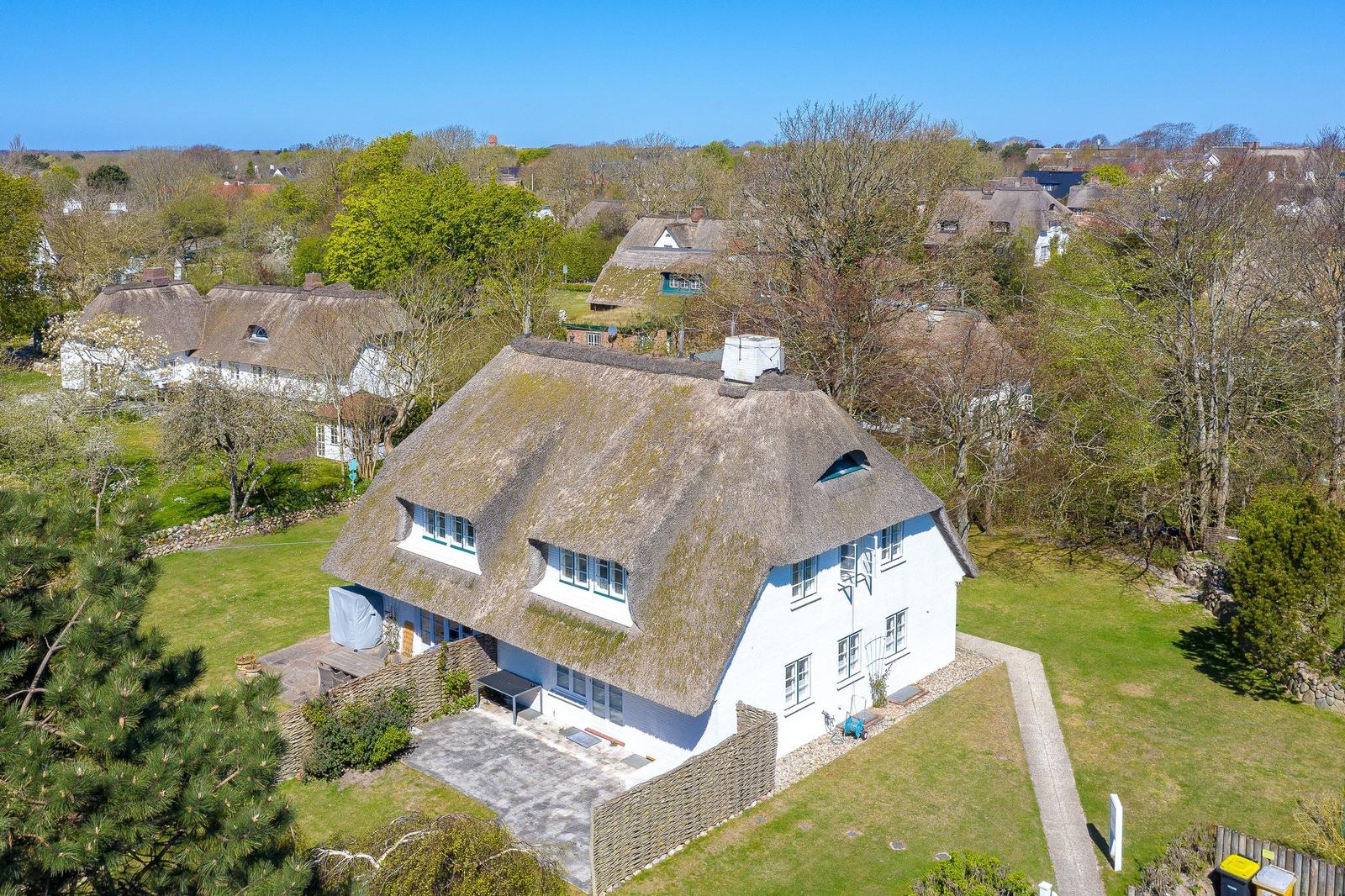 House with thatched roof and garden. Surrounded by trees and other houses.