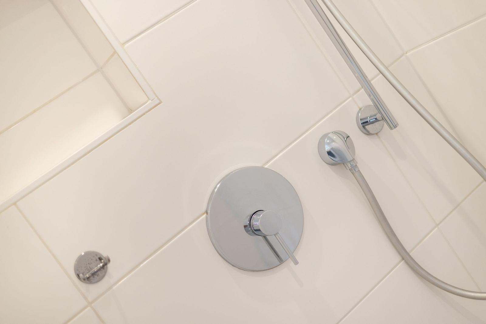 Dusche mit Chromarmatur und Handbrause an weißen Fliesen