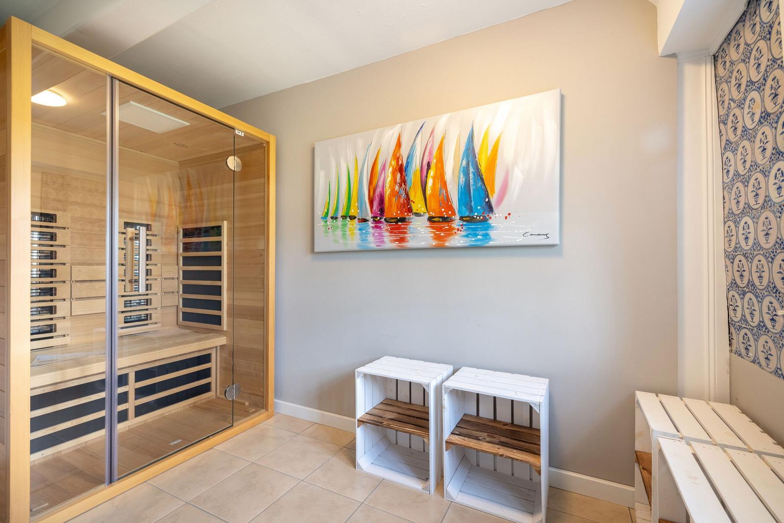 Sauna mit Glaswand, Wandbild mit Segelbooten und weiße Holzstühle.