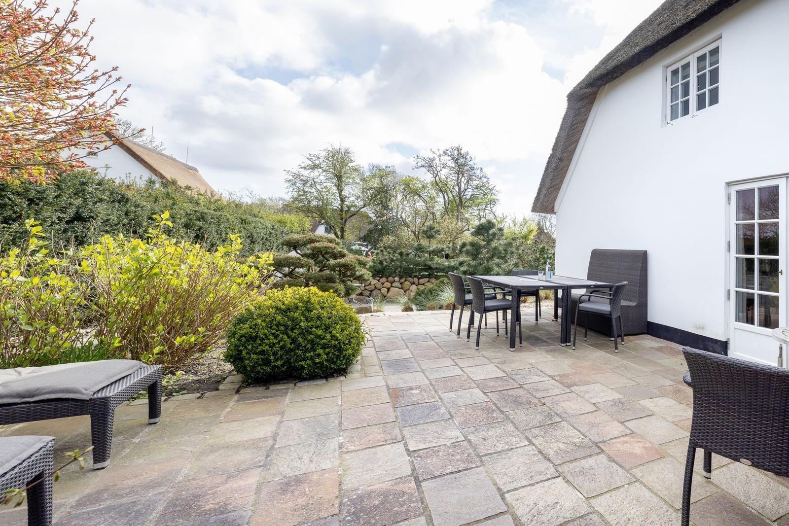 Terrasse mit Tisch, Stühlen und Gartenanlage neben einem Haus mit Schieferdach.