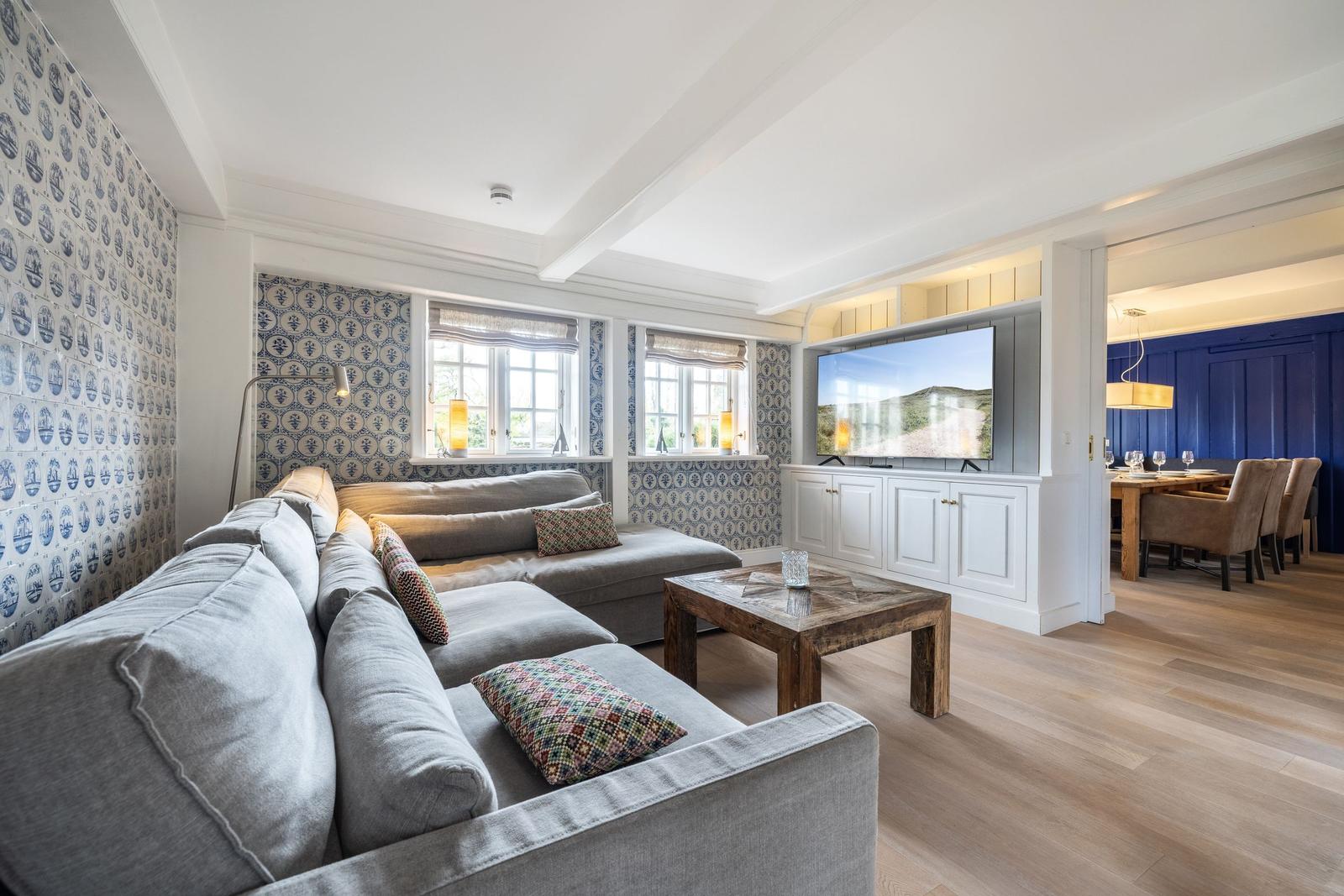 Wohnzimmer mit Sofa, Fernseher und Holzboden. Wand mit blau-weißem Muster.