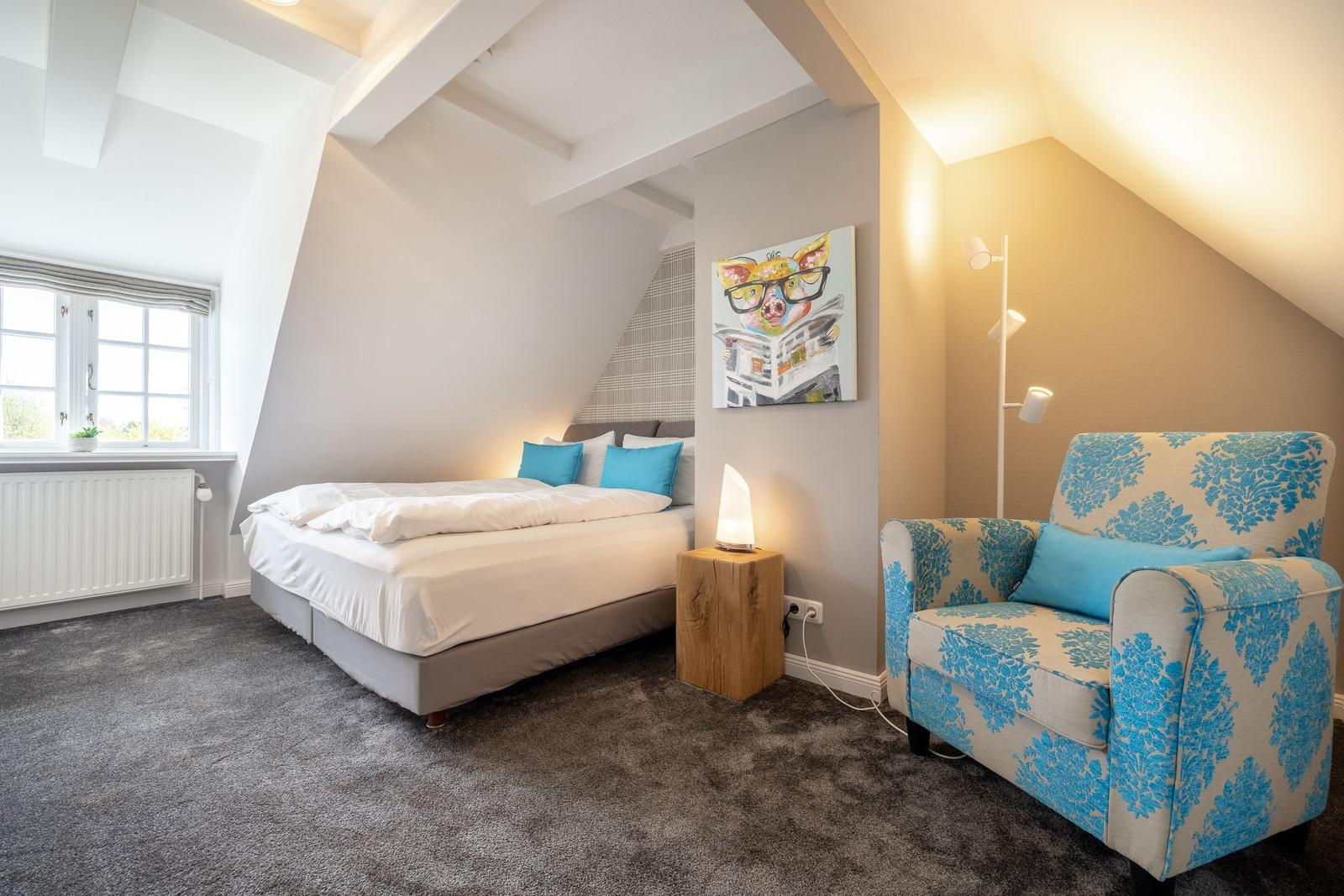 Schlafzimmer mit Bett, Sessel und Wandbild unter Dachschrägen.
