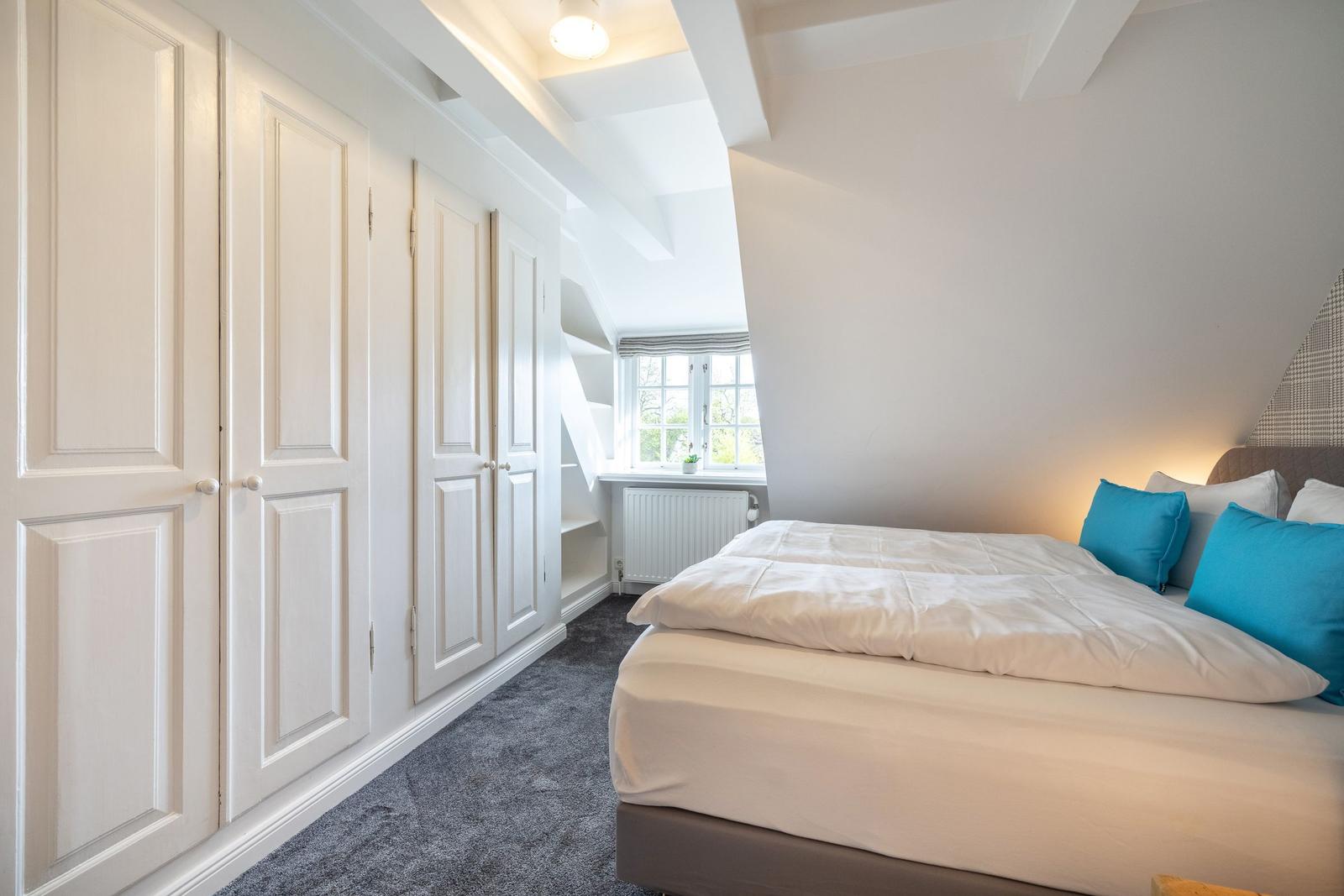 Schlafzimmer mit Doppelbett, Kleiderschrank und Fenster.
