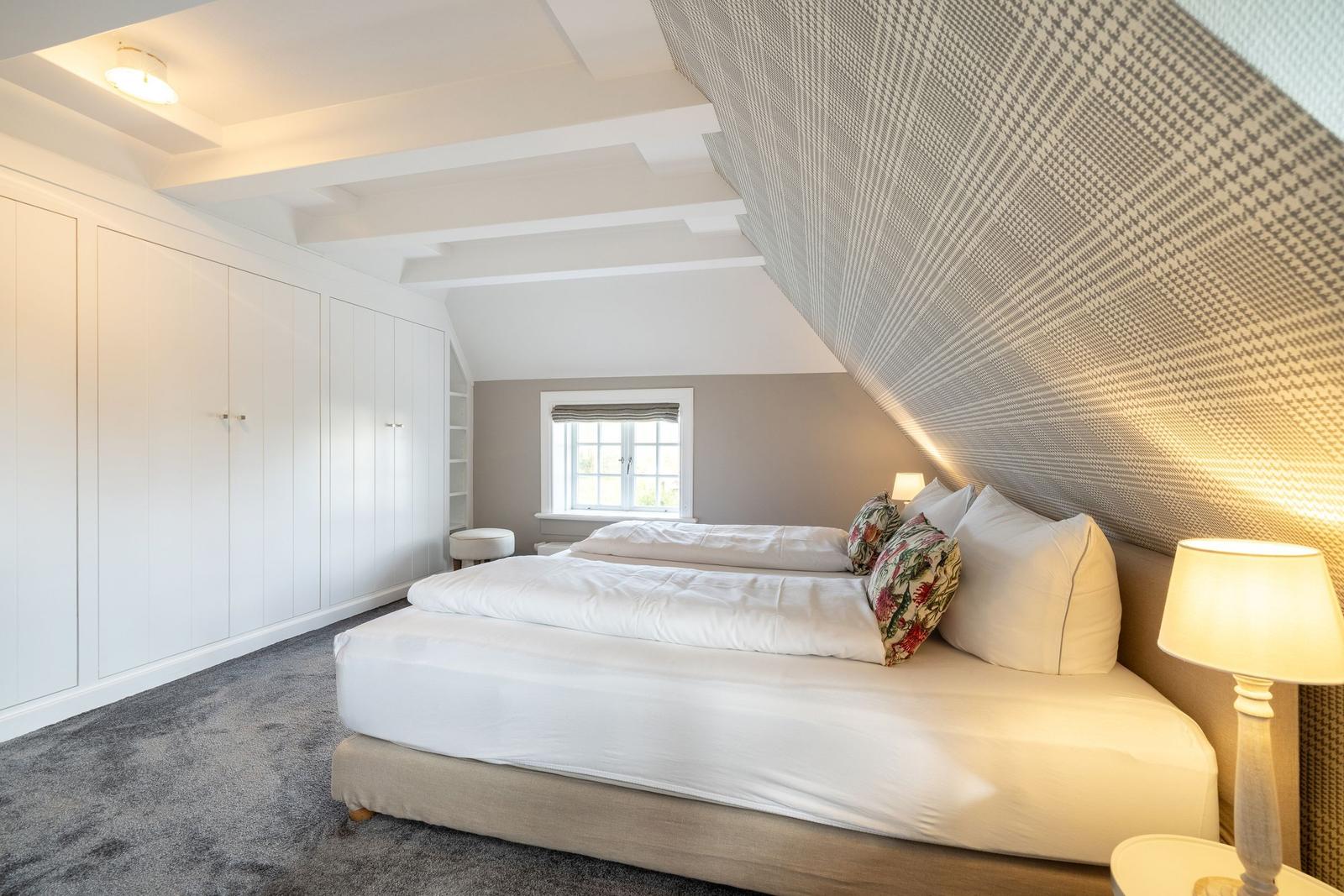 Schlafzimmer mit Dachschrägen, weißem Bett und Kleiderschrank