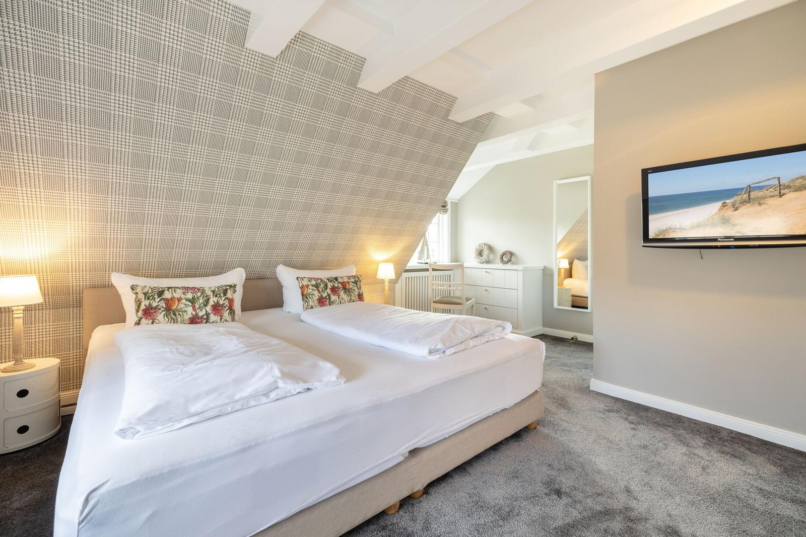 Schlafzimmer mit Doppelbett, TV und schräger Wandverkleidung.