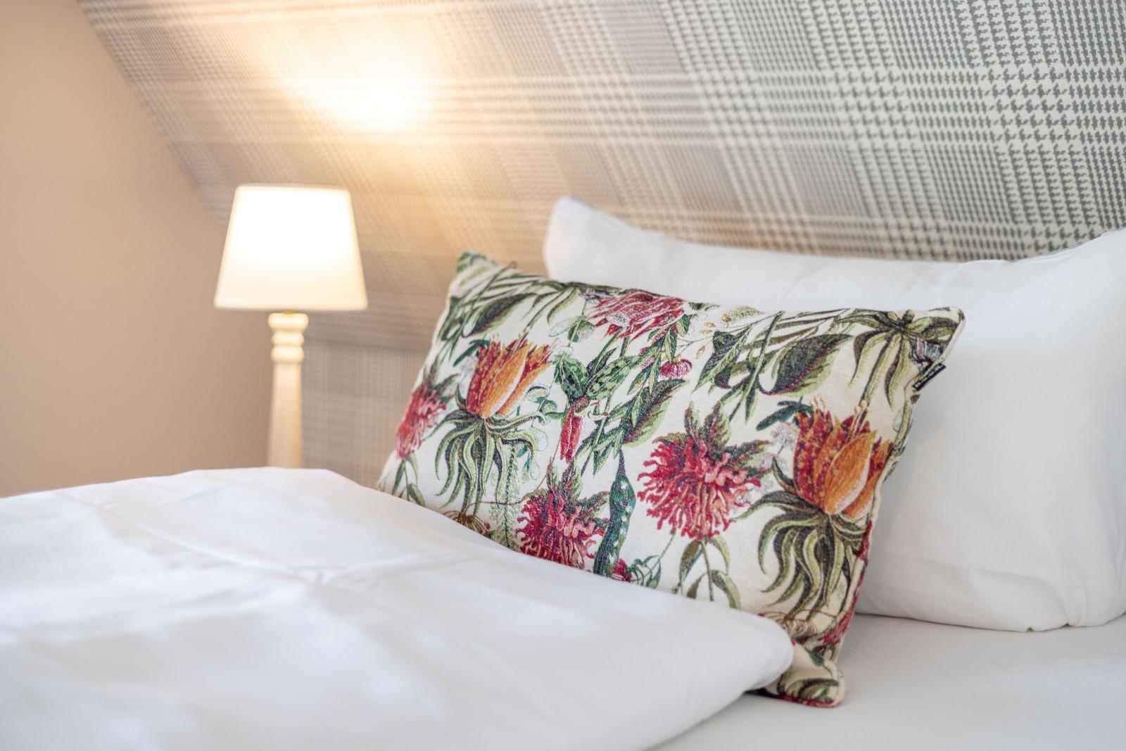 Bettkopfteil mit Muster, Kissen mit Blumenmotiv und Nachttischlampe.