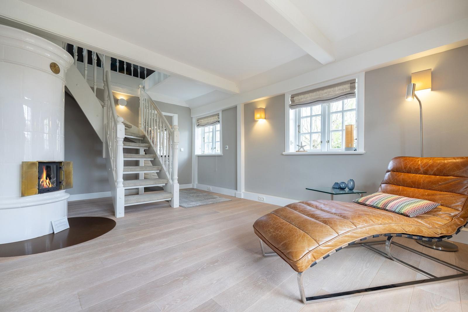 Wohnbereich mit Holzboden, brauner Ledercouch, Kamin und Treppe.