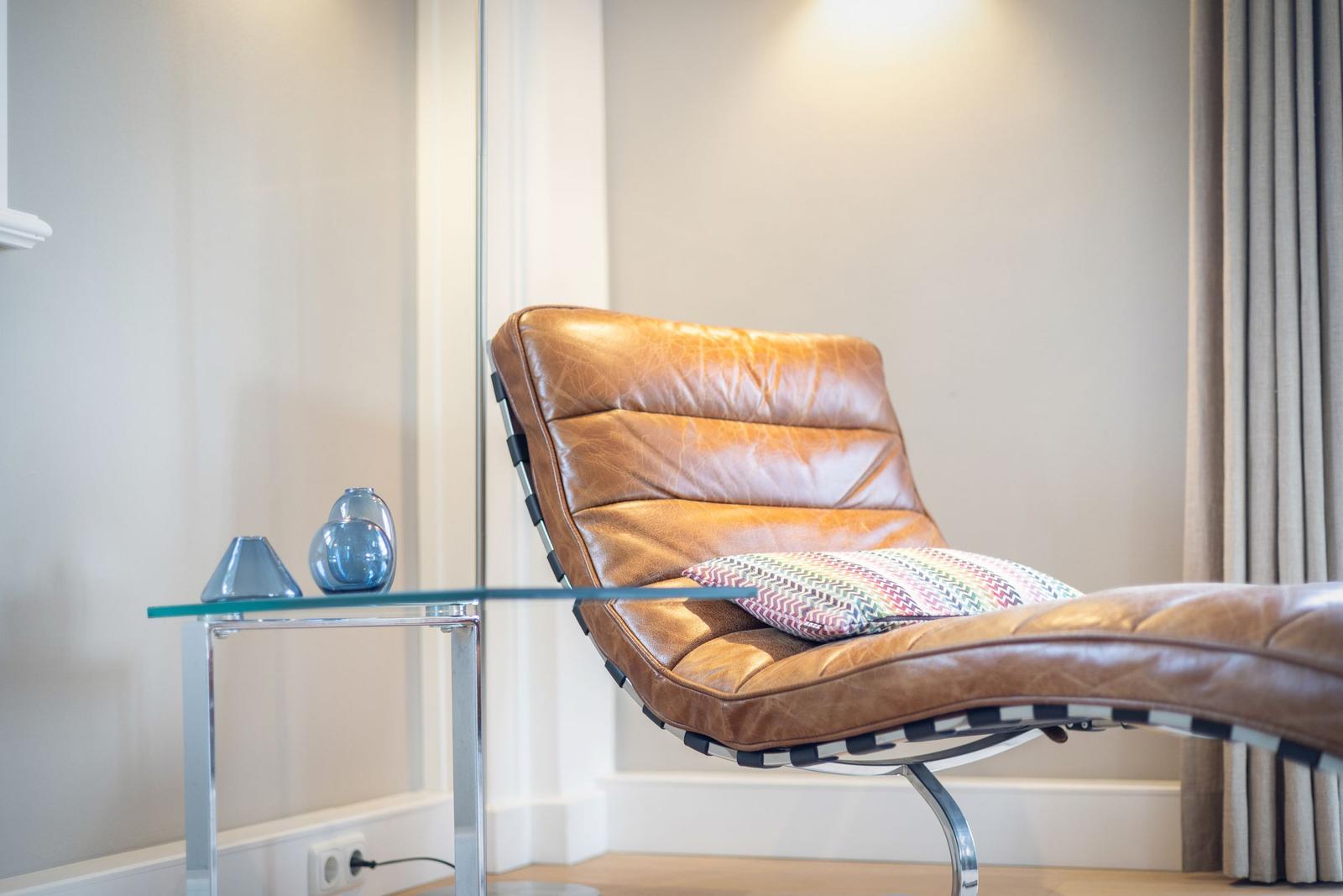 Brown leather lounge chair with patterned cushion beside glass table.