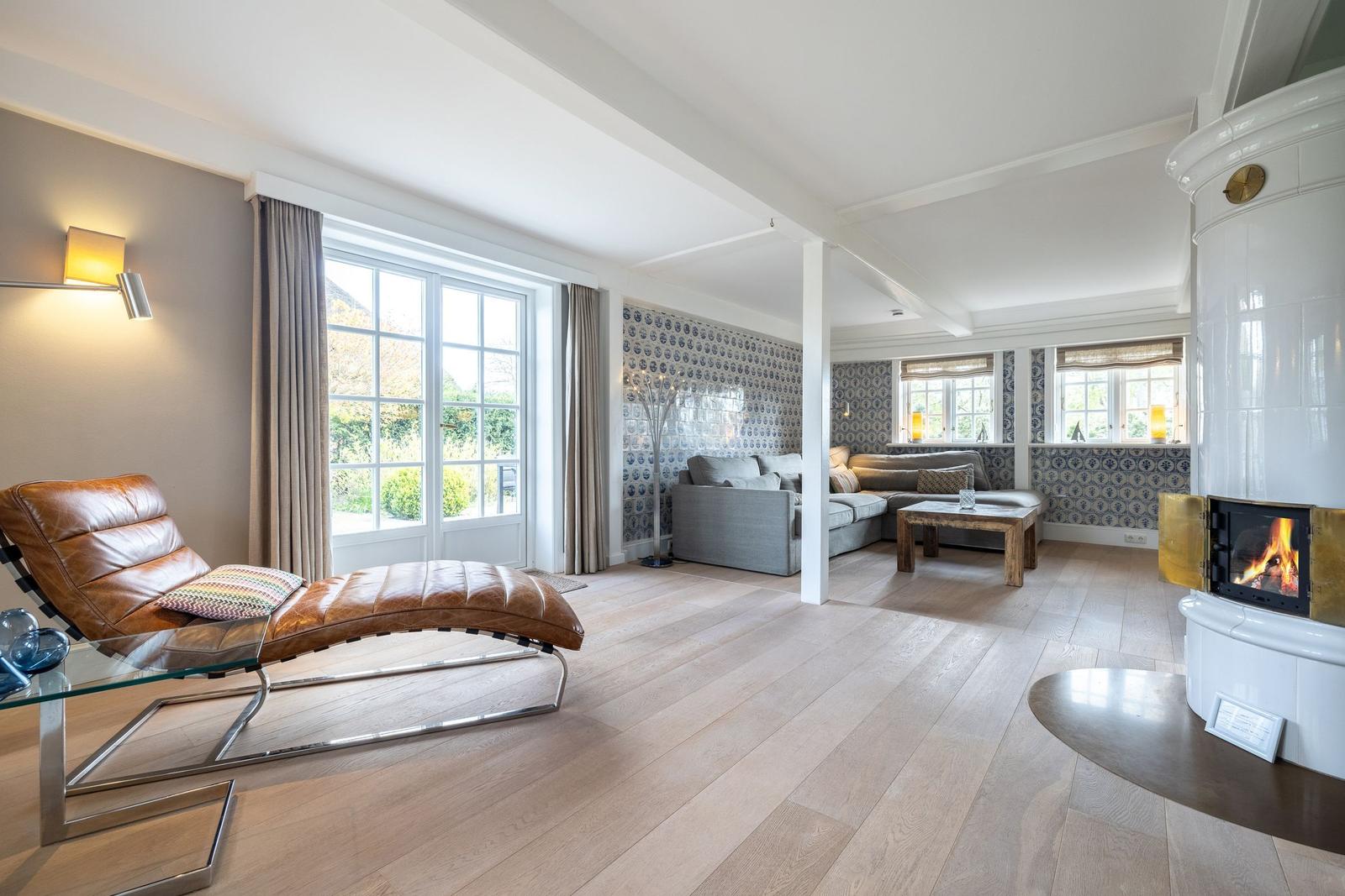 Wohnraum mit Lederliege, Kamin und Holzboden. Fenster mit Blick auf Garten.