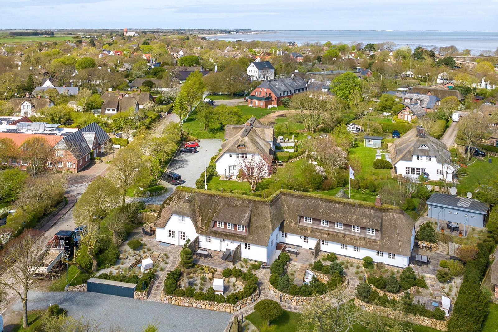 Traditionelles Ferienhaus mit Strohdach und Garten. Blick auf Küstenort mit Wasser im Hintergrund.