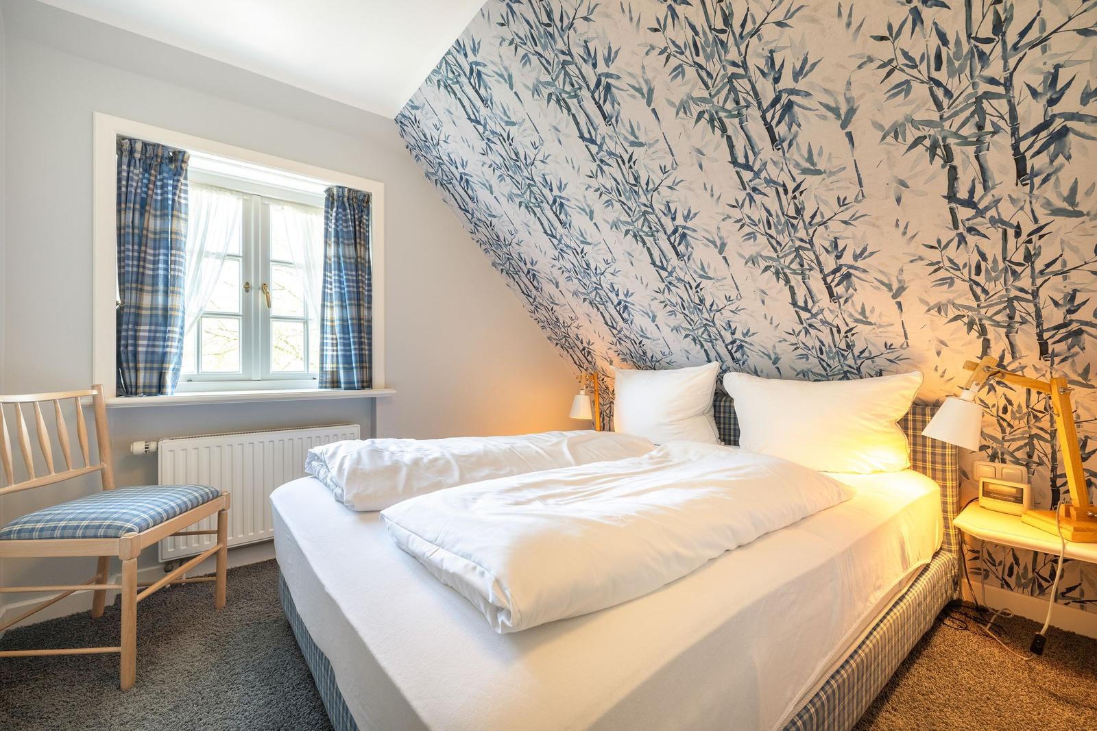 Schlafzimmer mit Bett, Fenster und Tapete mit Bambusmotiv.
