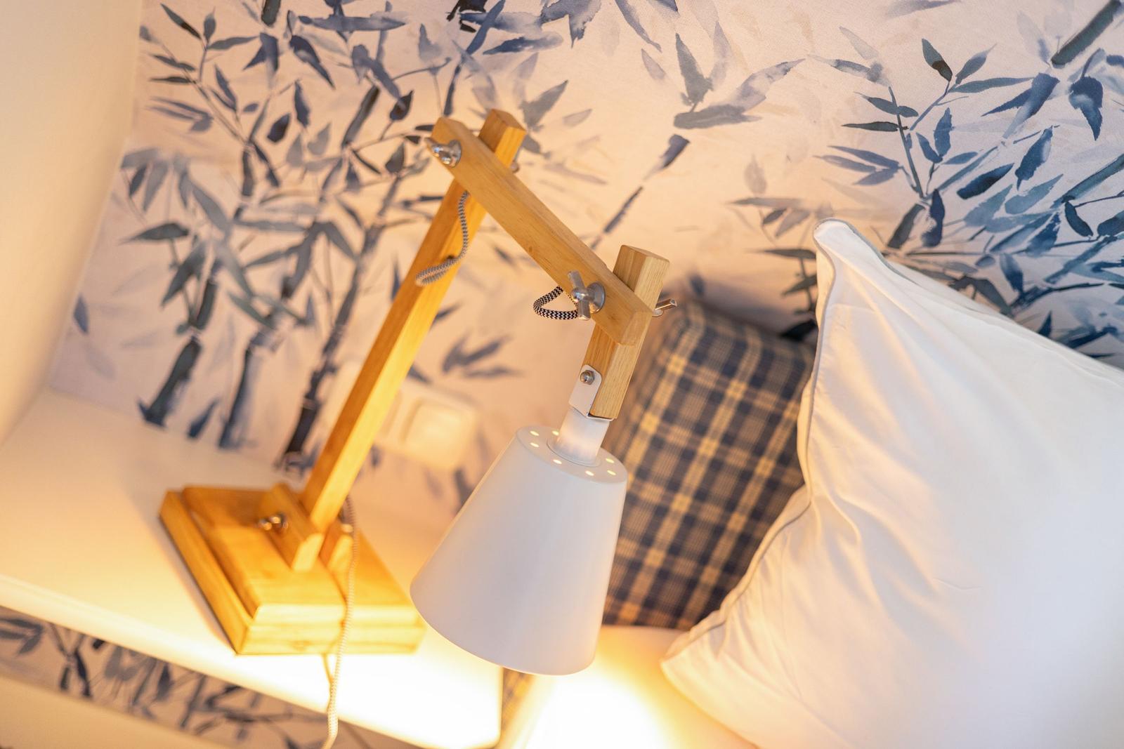 Nachtisch mit Holzlampe und Kissen vor blau-weißem Tapetenmuster.